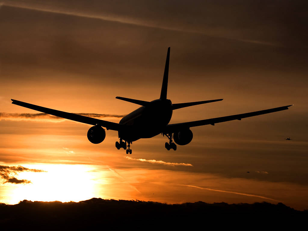 Airport 桌布 壁紙 — 一架商用飛機在降落時，以火紅的日落天空為背景形成剪影。