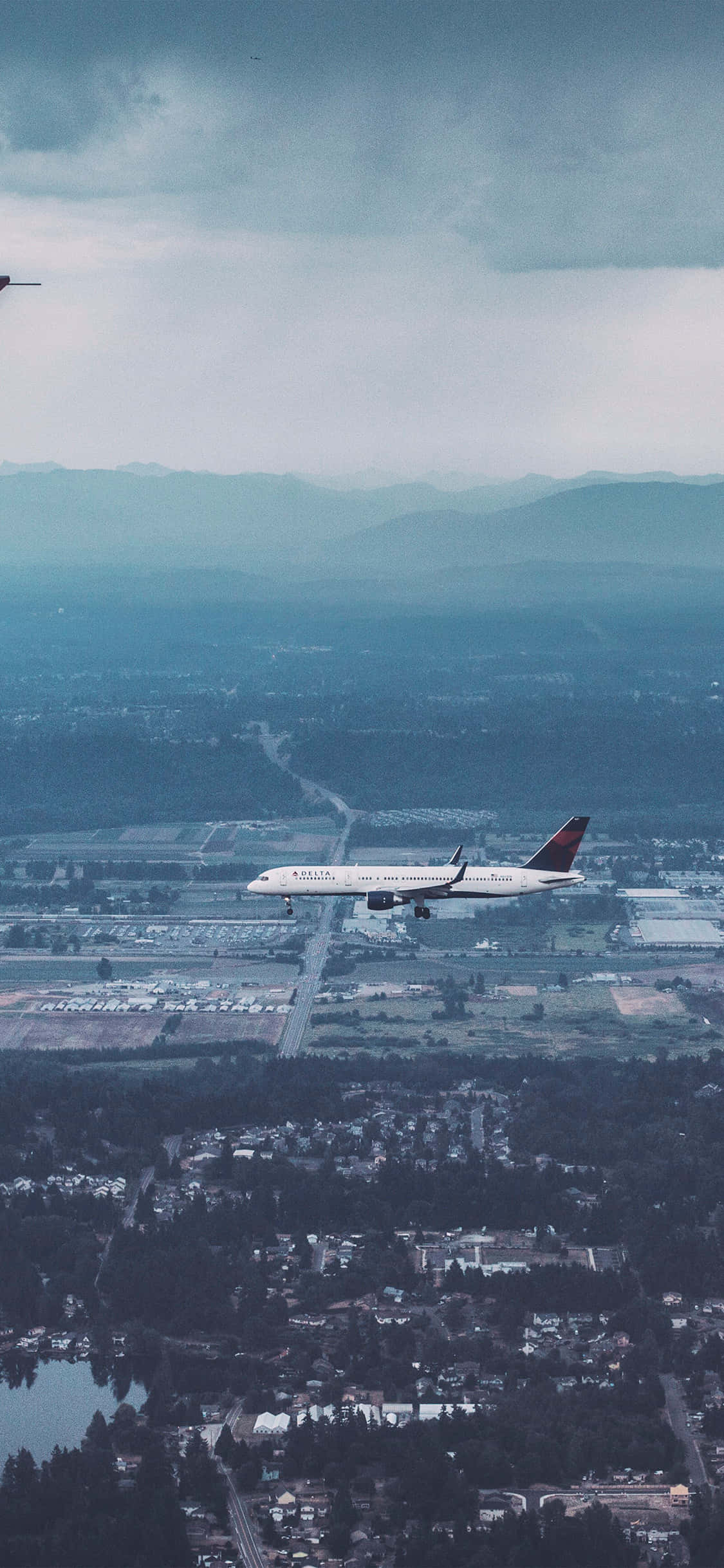 Airlines 桌布 壁紙 — 一架商用飛機在陰沉多雲的天空下，向著遠處有山巒的機場跑道下降。