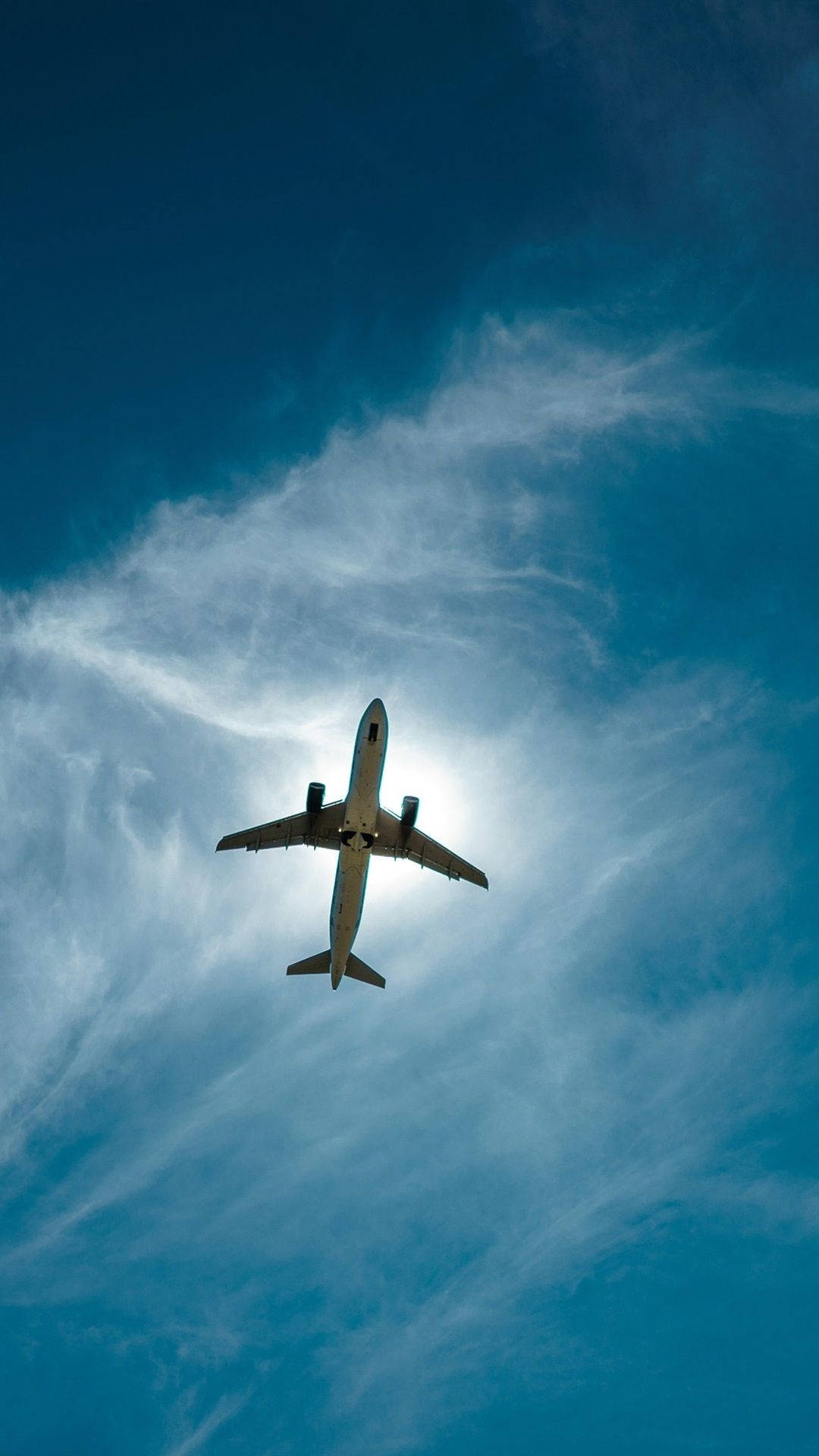 Plane 桌布 壁紙 — 一架商用飛機在陽光映照下，從下方仰望，翱翔於帶有縷縷白雲的湛藍天空。