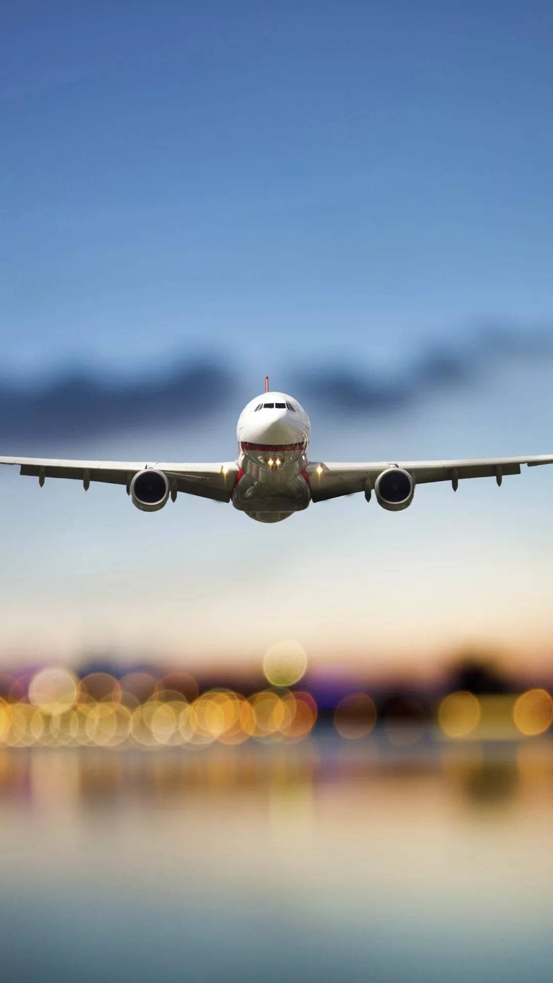 飛機 桌布 壁紙 — 一架商用飛機在黃昏時分向城市景觀下降，下方有模糊的金色散景燈光。