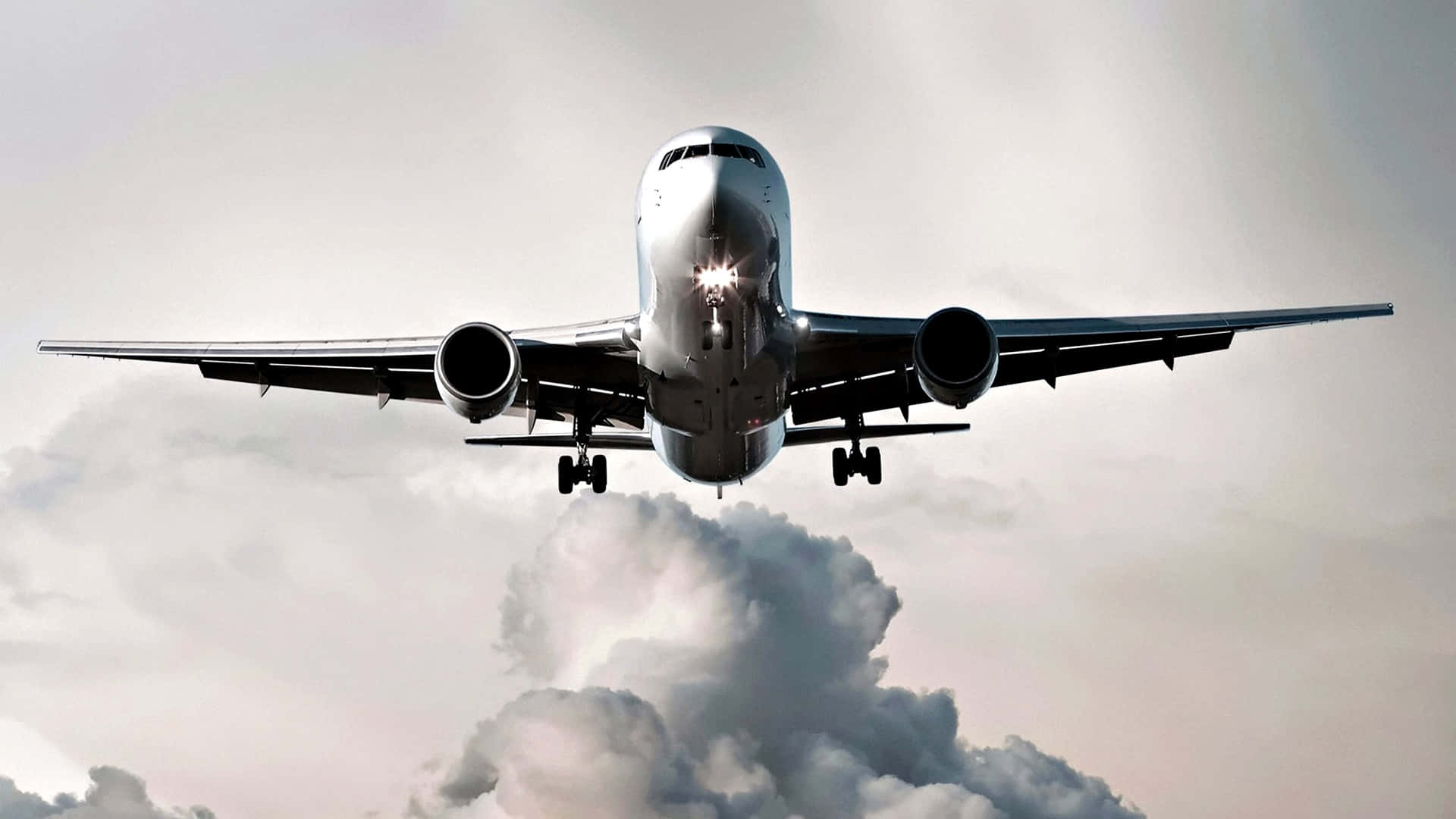 HD Plane 桌布 壁紙 — 一架商用飛機正放下起落架，在柔和灰色天空的背景下向雲層下降。
