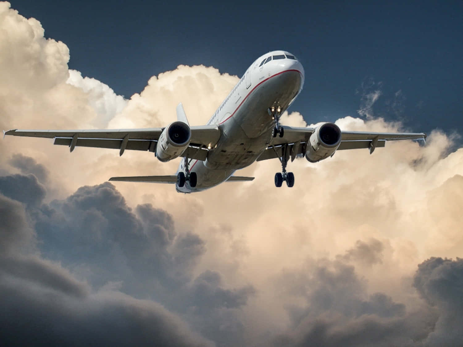 飛機 桌布 壁紙 — 一架商用飛機穿過戲劇性的雲層下降，起落架放下，背景是陰沉天空。