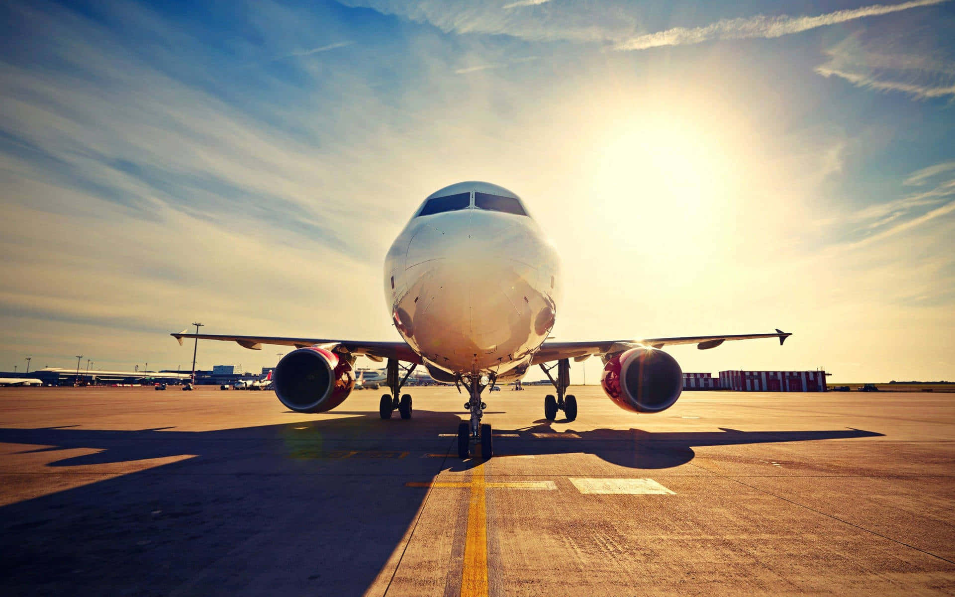 飛機 桌布 壁紙 — 一架商用飛機面向鏡頭，停在陽光普照的停機坪上，機頭後方閃耀著金色光芒。