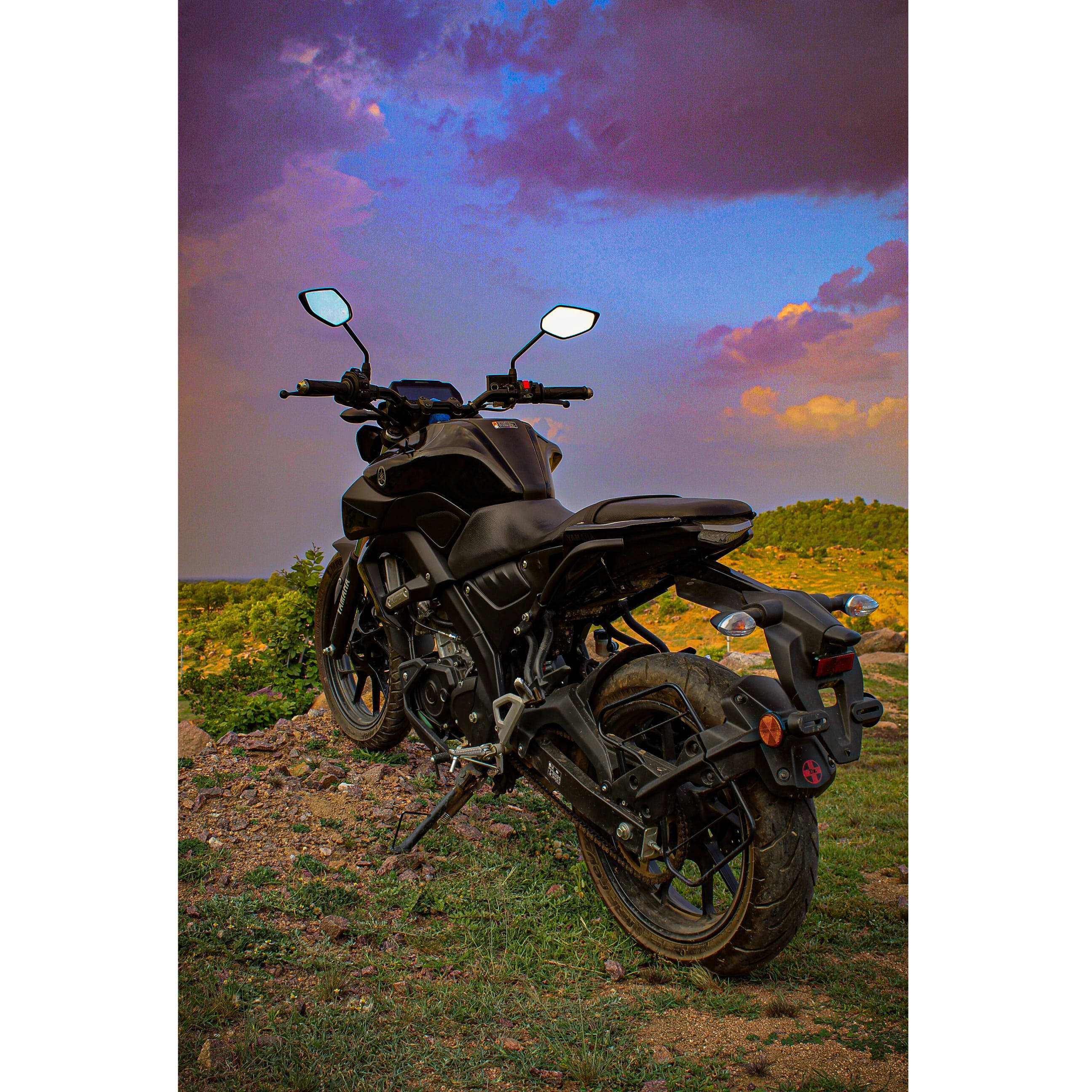 yamaha mt 15 桌布 壁紙 — 一架啞光黑色機車停在草地上，背景是戲劇性的紫色和橙色日落天空。