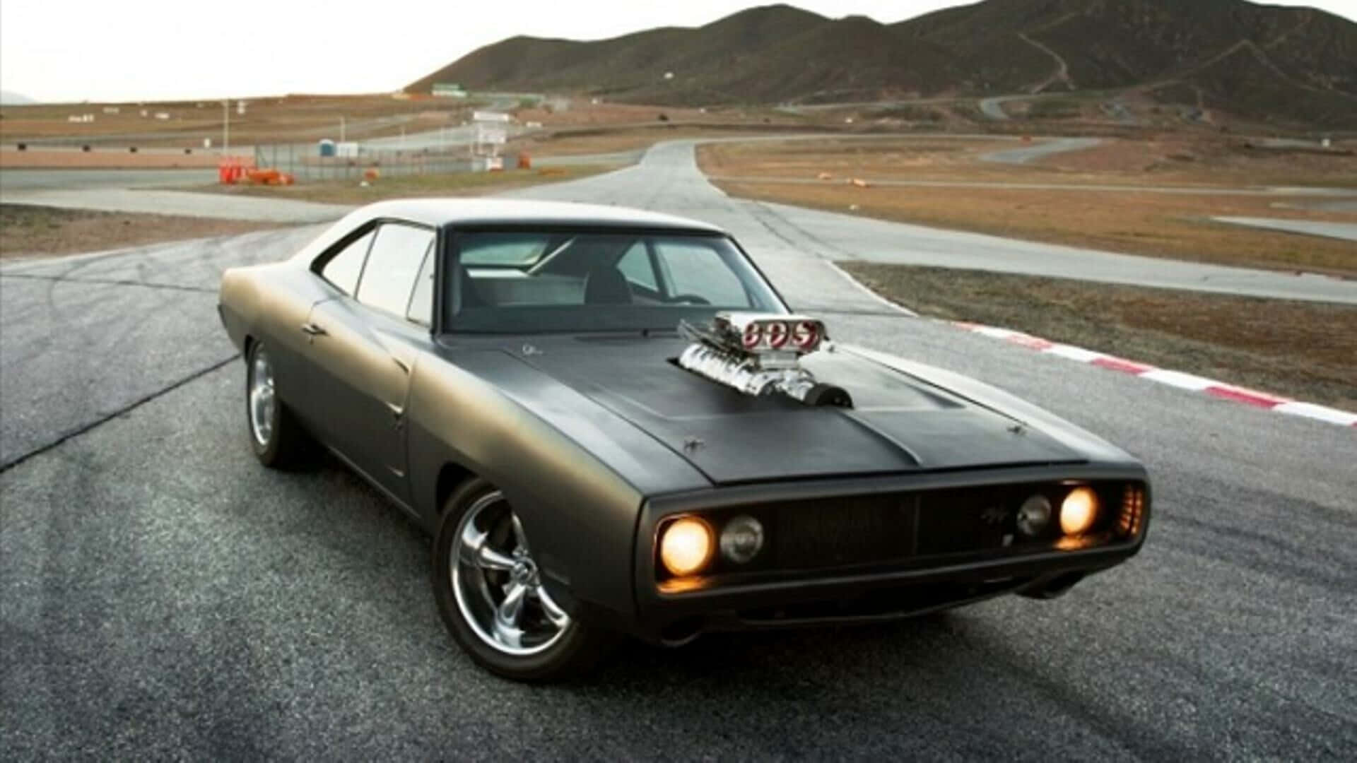 Fast And Furious 1 桌布 壁紙 — 一架啞光黑色經典肌肉車配備增壓器，在黃昏時分停在賽道上，背景有山丘。
