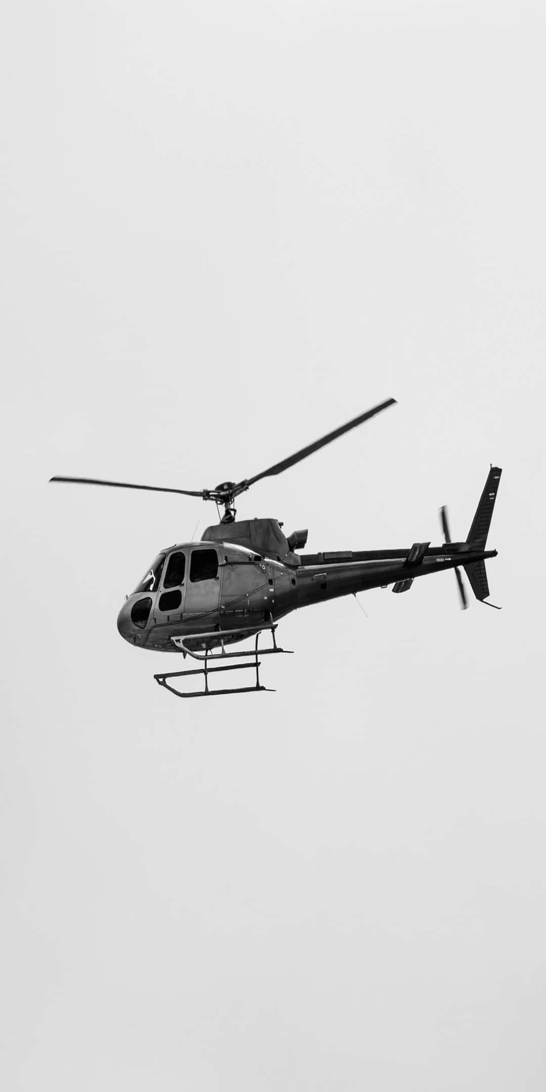 Helicopter 桌布 壁紙 — 一架單色直升機在蒼白的陰天中翱翔，旋翼在極簡背景下旋轉。