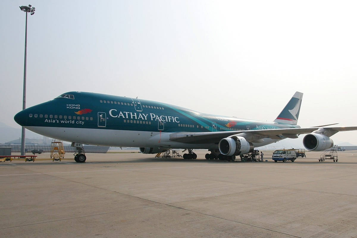Airport 桌布 壁紙 — 一架國泰航空波音747停泊在機場停機坪上，天空多雲，附近有地勤人員和設備。