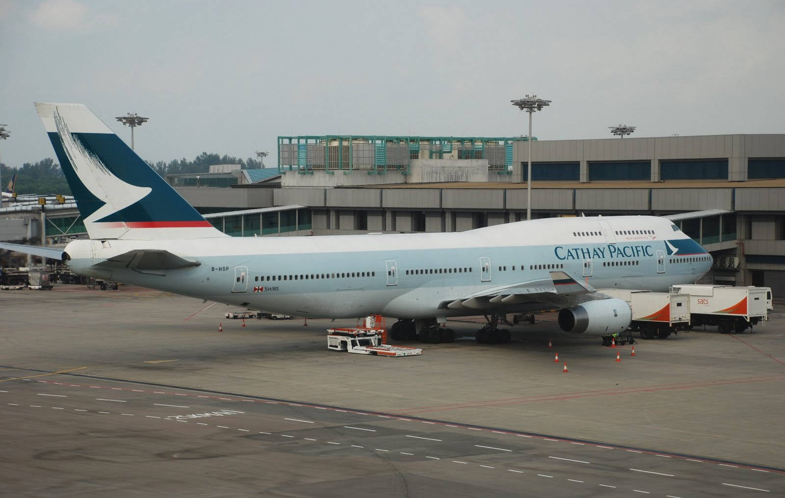 Airport 桌布 壁紙 — 一架國泰航空波音747停泊在機場閘口，附近有地勤人員和設備，天空多雲。