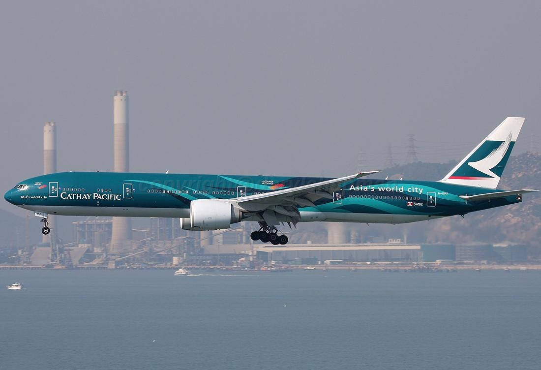 飛機 桌布 壁紙 — 一架國泰航空波音777以青綠色塗裝在水面上降落，背景有朦朧的工業煙囪。