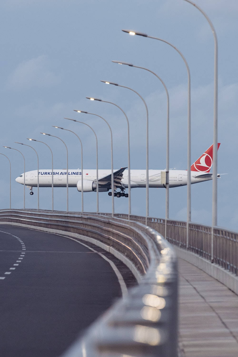 Airport 桌布 壁紙 — 一架土耳其航空飛機在淡藍色天空下，低空飛過一條有路燈的彎曲高速公路。
