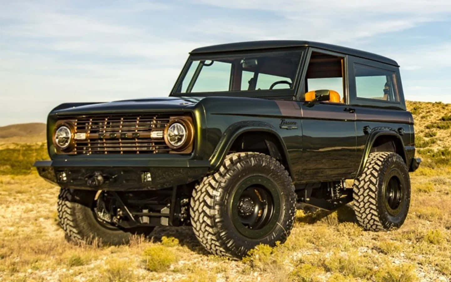 Ford Bronco 桌布 壁紙 — 一架堅固的深綠色復古福特Bronco，配備超大輪胎，驕傲地矗立在陽光明媚的沙漠景觀中。