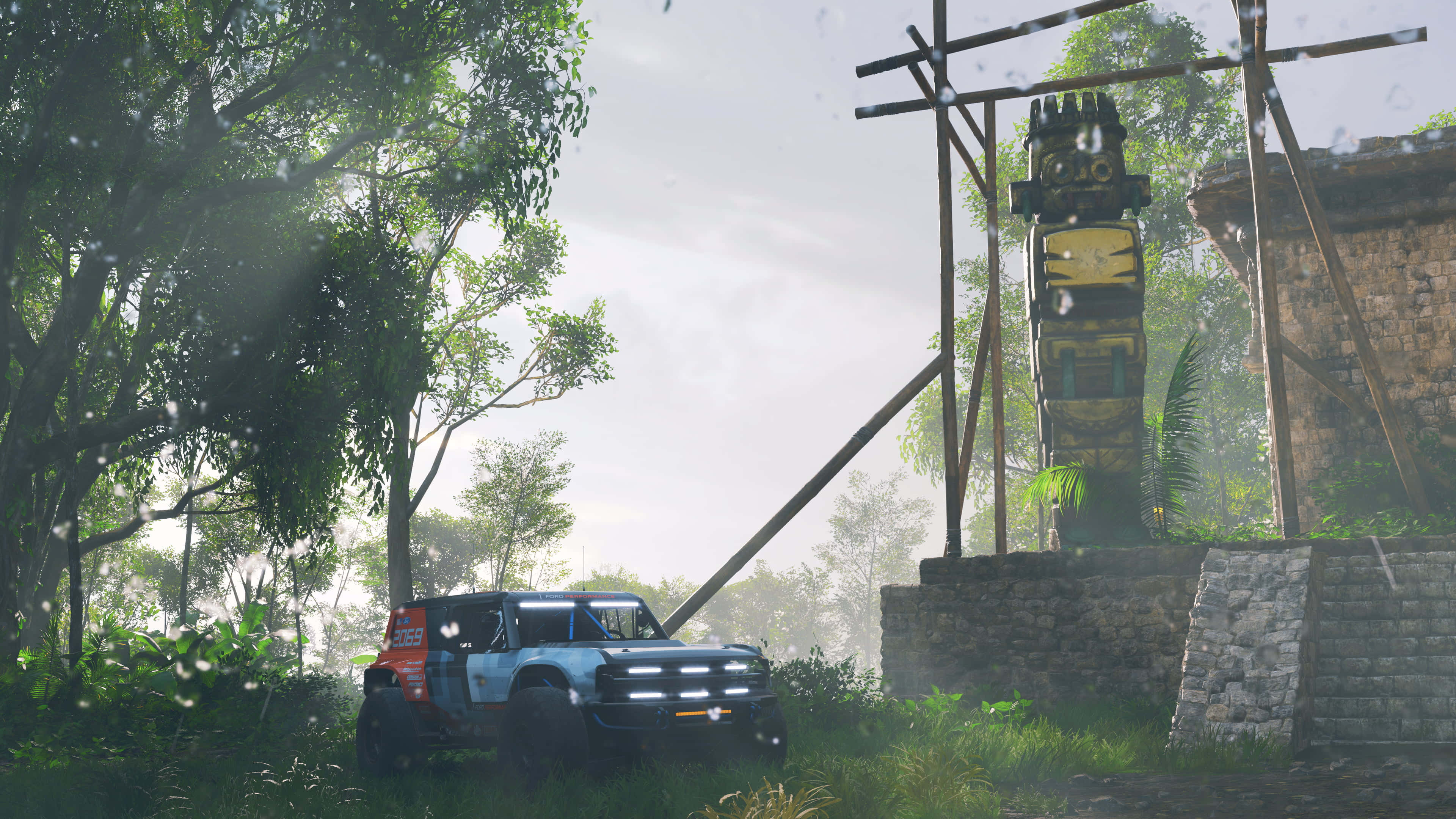 Forza Horizon 5 4K 桌布 壁紙 — 一架堅固的藍色拉力賽車停泊在霧氣瀰漫的叢林空地上，旁邊有一個古老的石圖騰。