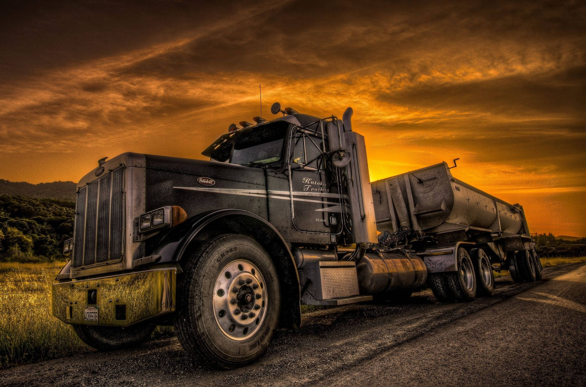 Peterbilt 桌布 壁紙 — 一架堅固的黑色半掛卡車連油罐拖車在鄉村道路上休息，背景是火紅的橙色日落天空。