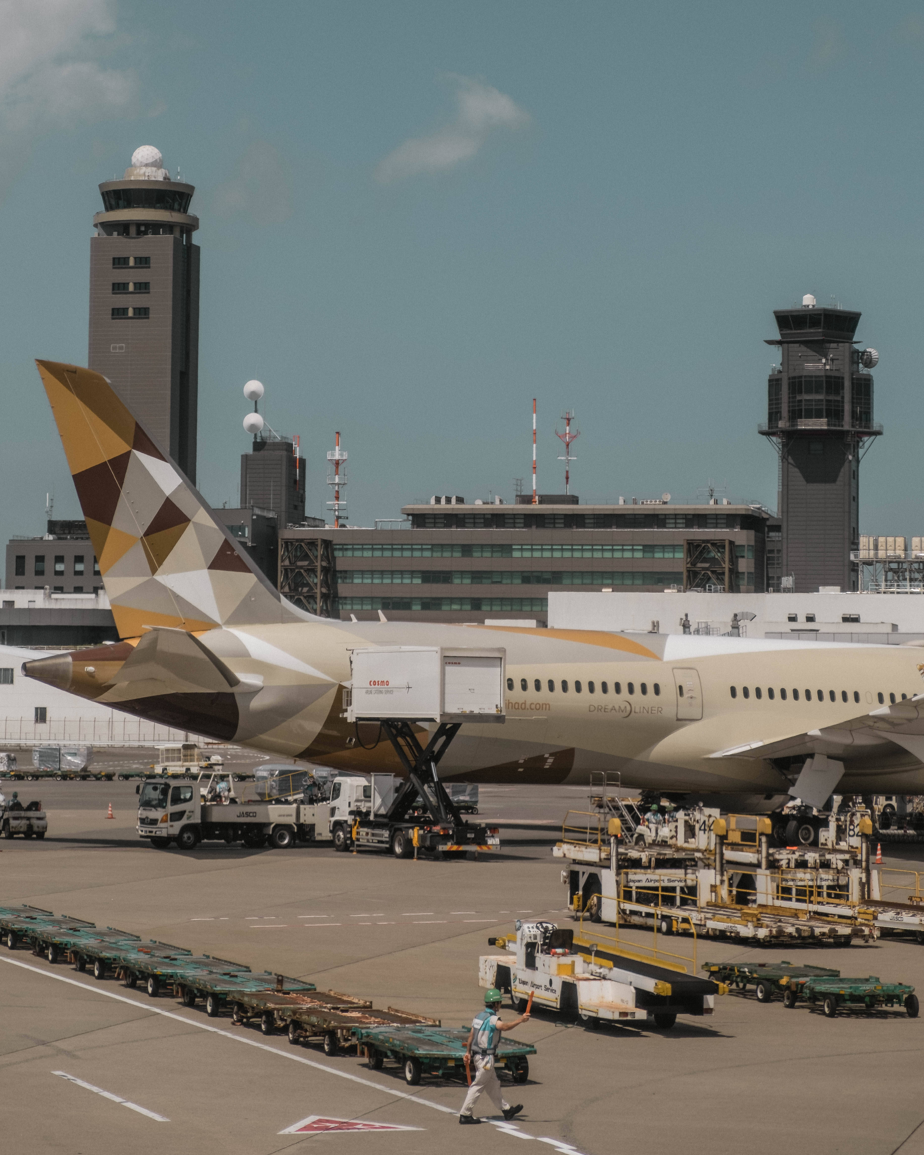 Plane 桌布 壁紙 — 一架塗有幾何金色和米色塗裝的夢幻客機停在機場閘口，地勤人員和設備在晴朗的藍天下。