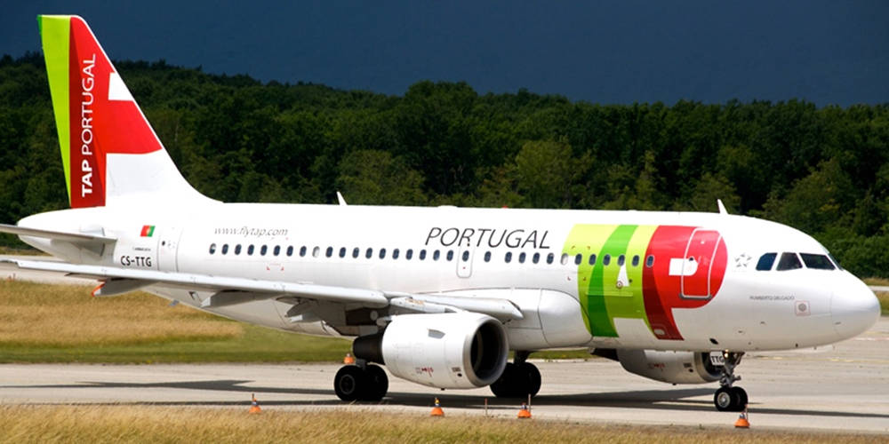 Airport 桌布 壁紙 — 一架塗有紅、綠、白色塗裝的TAP Portugal飛機在黑暗天空和森林覆蓋的山坡背景下在跑道上滑行。