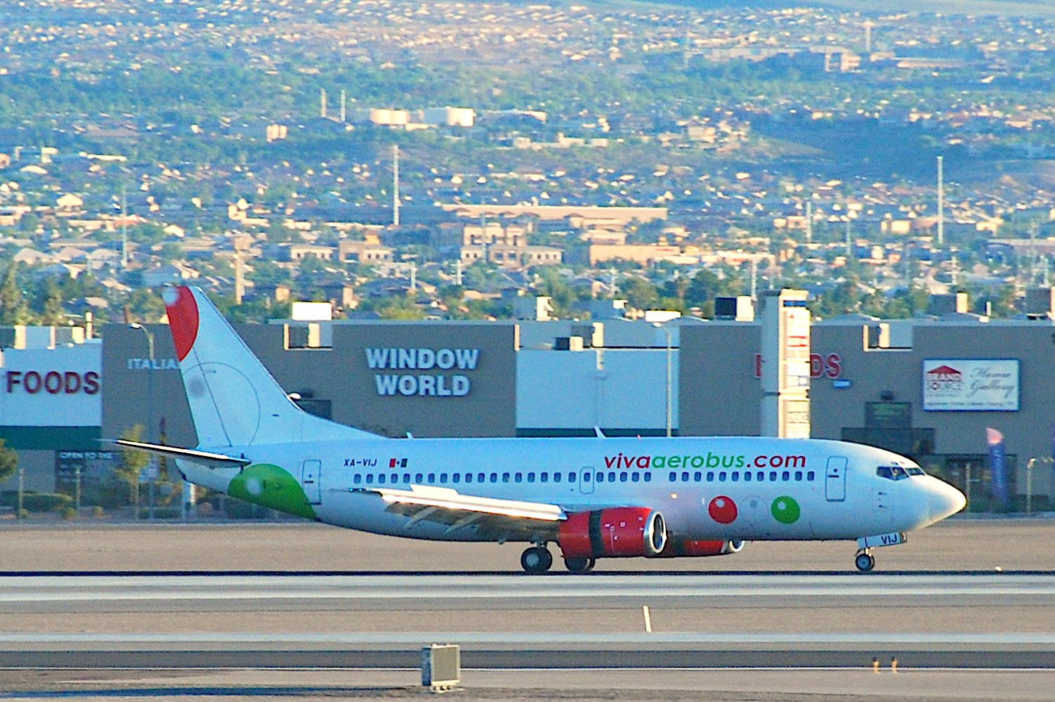 Airport 桌布 壁紙 — 一架塗有紅、綠、白色塗裝的Viva Aerobus飛機在跑道上滑行，背景是廣闊的郊區景觀。