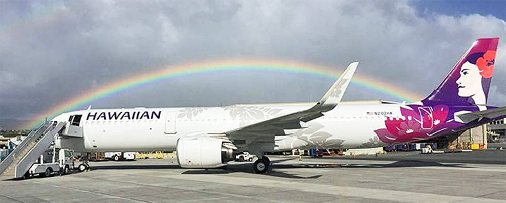 彩虹 桌布 壁紙 — 一架夏威夷航空的飛機停在停機坪上，一道鮮豔的彩虹橫跨多雲的天空。