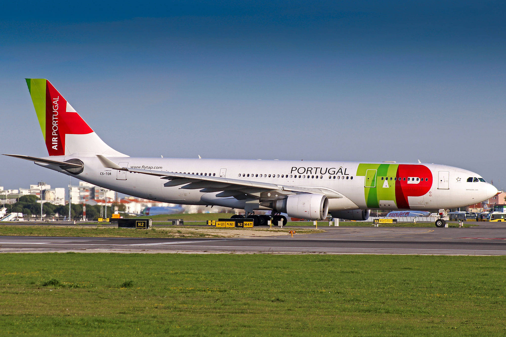 Airport 桌布 壁紙 — 一架大型Air Portugal飛機，帶有綠色、紅色和白色塗裝，在晴朗藍天下於跑道上滑行。