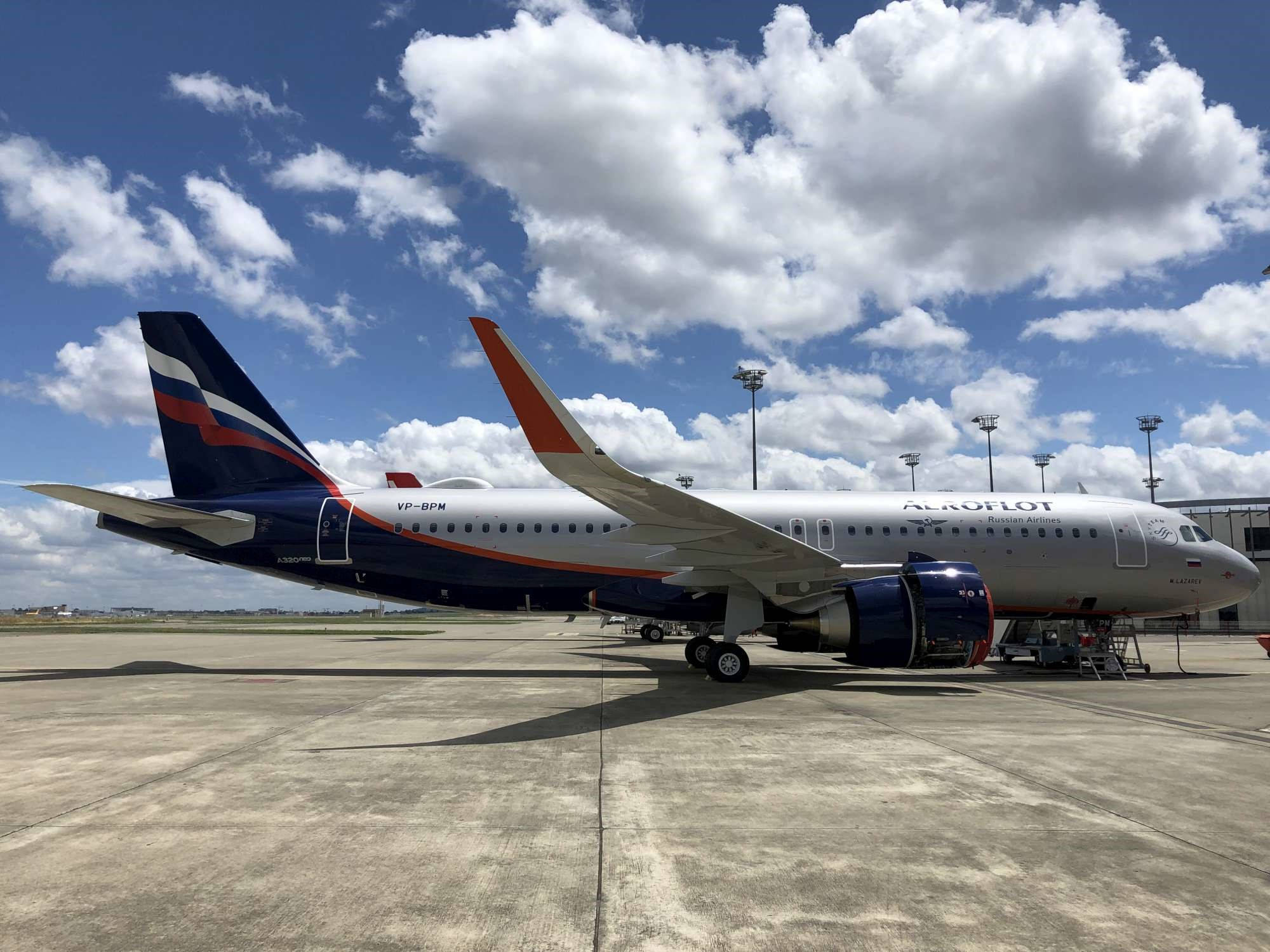 Airport 桌布 壁紙 — 一架大型俄航飛機，採用藍、紅、白塗裝，停在陽光明媚的停機坪上，天空湛藍，白雲朵朵。