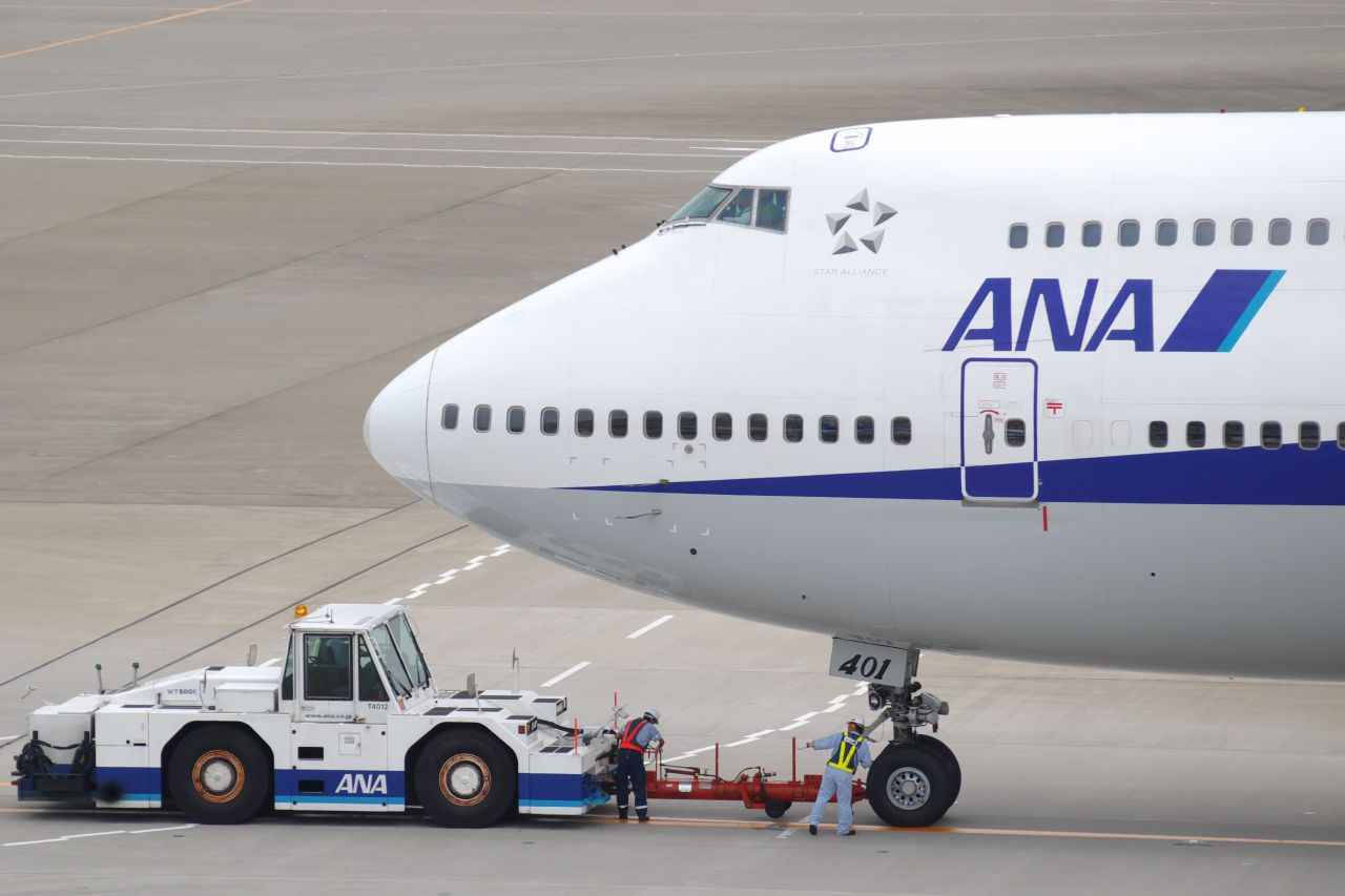 Truck 桌布 壁紙 — 一架大型全日空飛機正在灰色停機坪上被地面拖車推動，附近有地勤人員。
