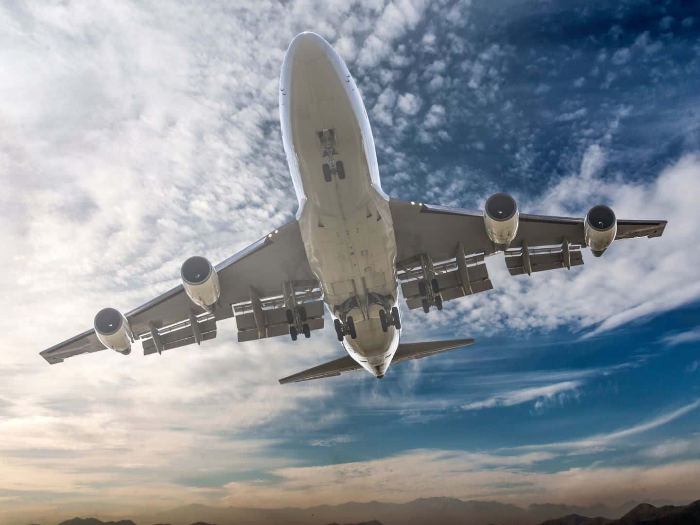 飛機 桌布 壁紙 — 一架大型商用飛機在藍白雲朵的戲劇性天空背景下，放下起落架從頭頂飛過。
