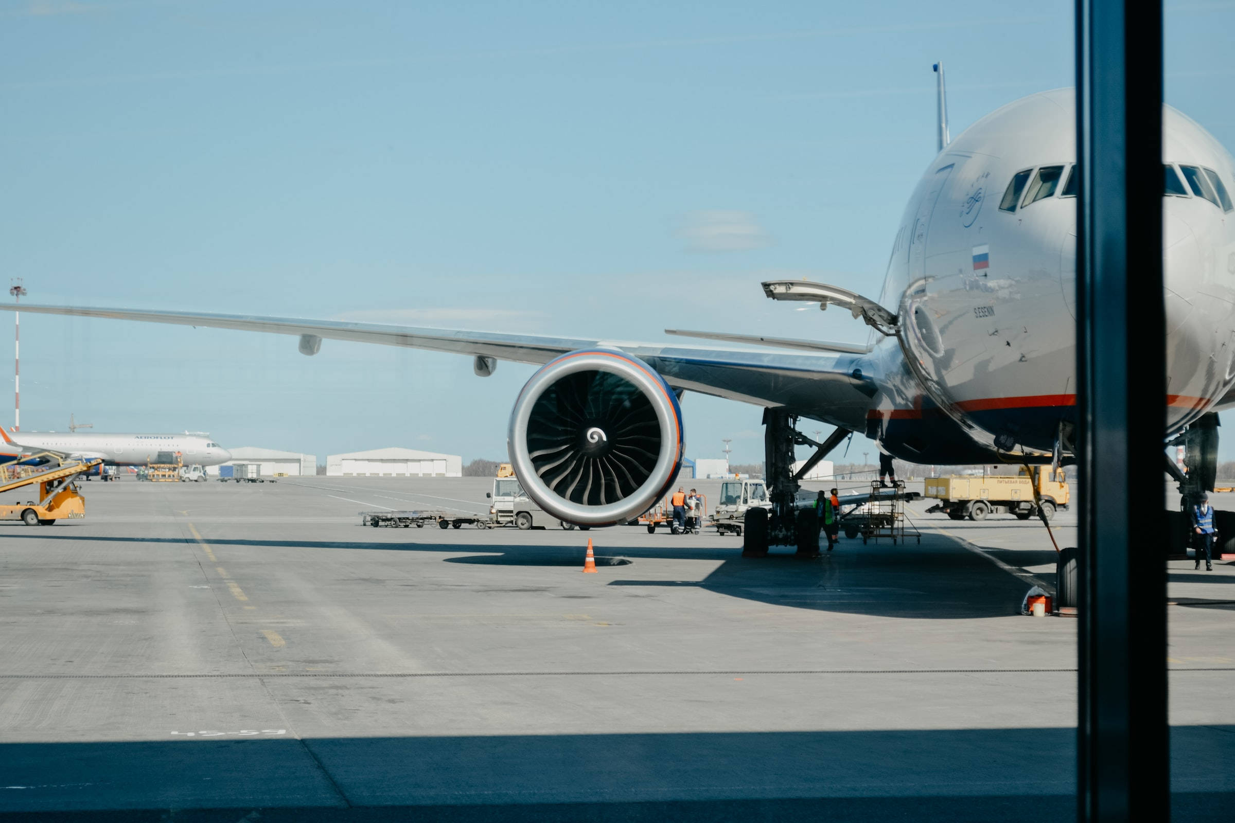 飛機 桌布 壁紙 — 一架大型客機停在停機坪上，天空晴朗蔚藍，附近有地勤人員和設備。
