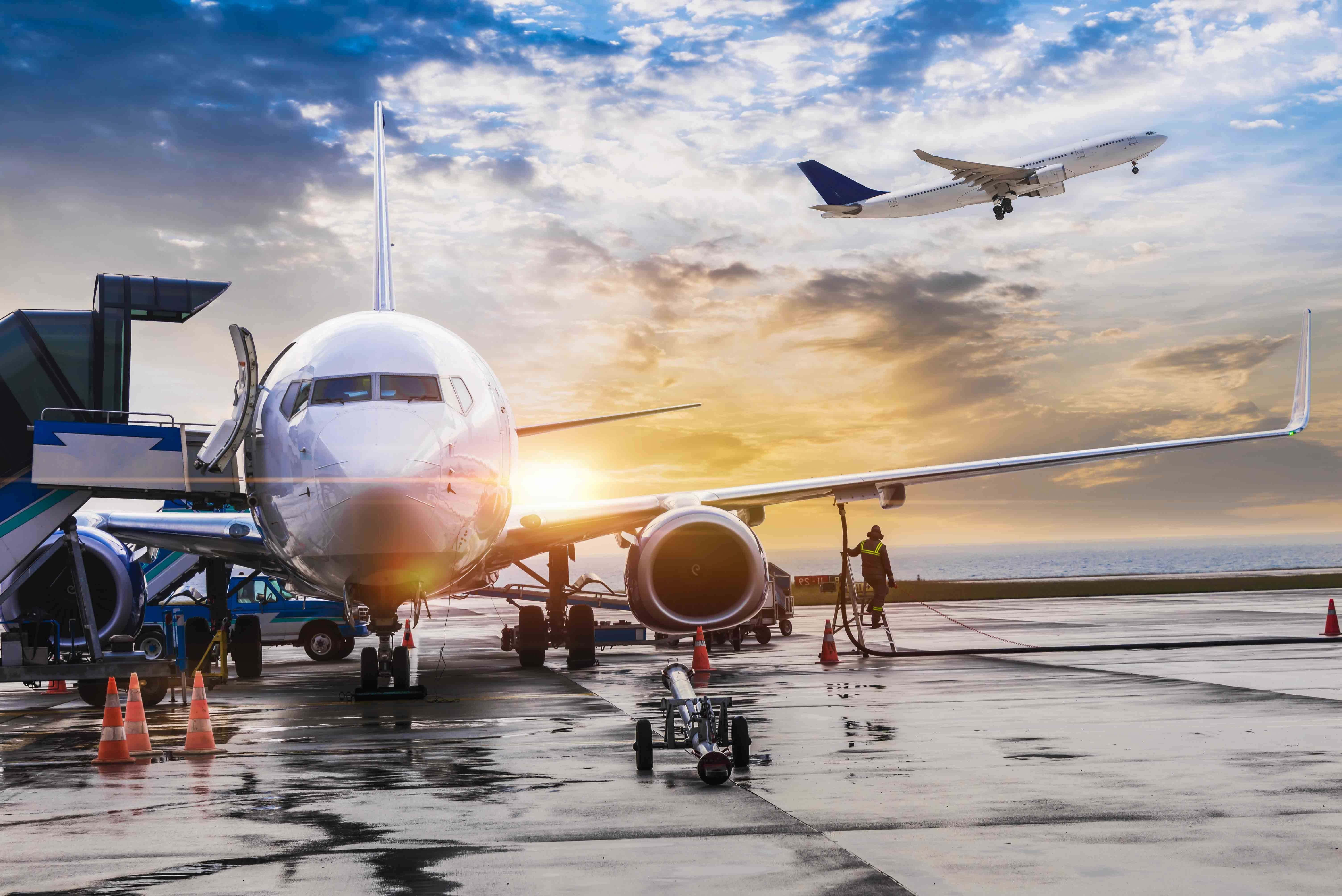 航太 桌布 壁紙 — 一架大型客機停在機場閘口，另一架飛機正升向金色的日落天空。