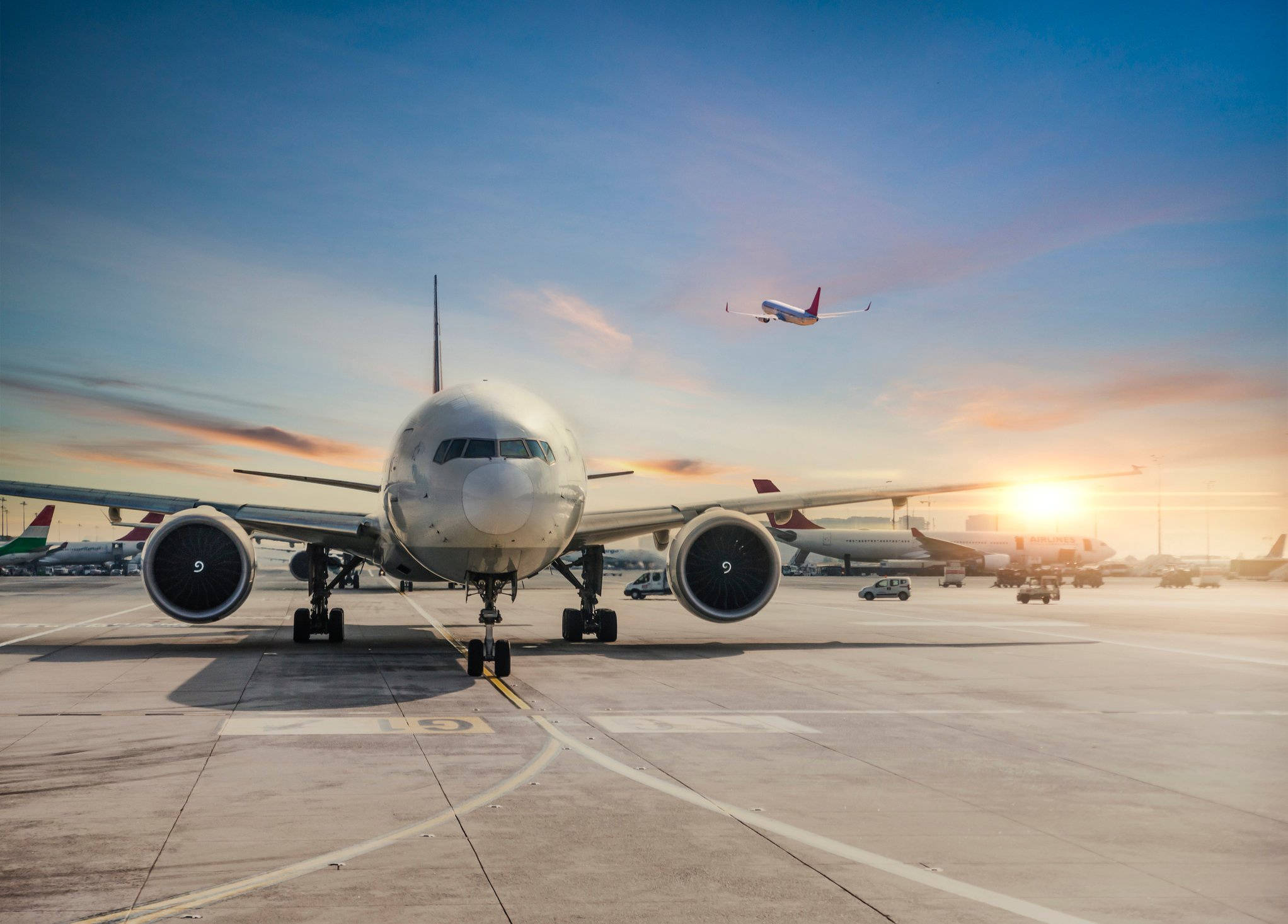 Airport 桌布 壁紙 — 一架大型客機在日落時分停在機場停機坪上，另一架飛機正升入色彩繽紛的天空。