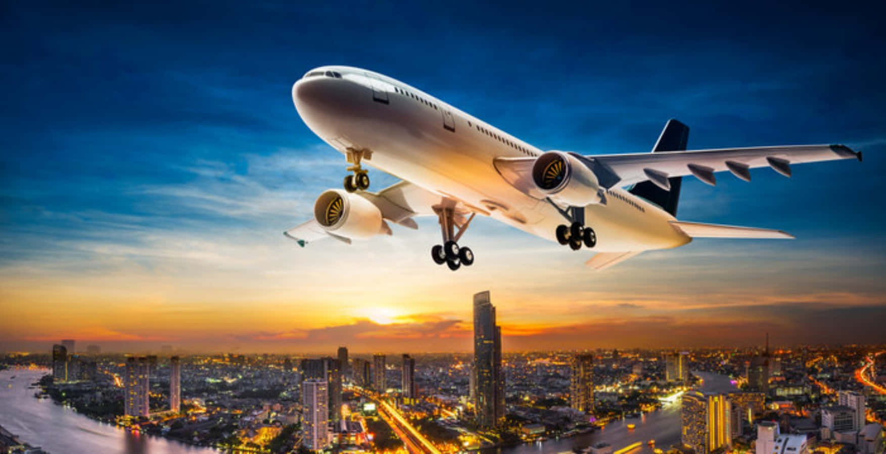 飛機 桌布 壁紙 — 一架大型客機在日落時分降落在廣闊的城市景觀上，閃爍的燈光和蜿蜒穿過城市範圍的河流。