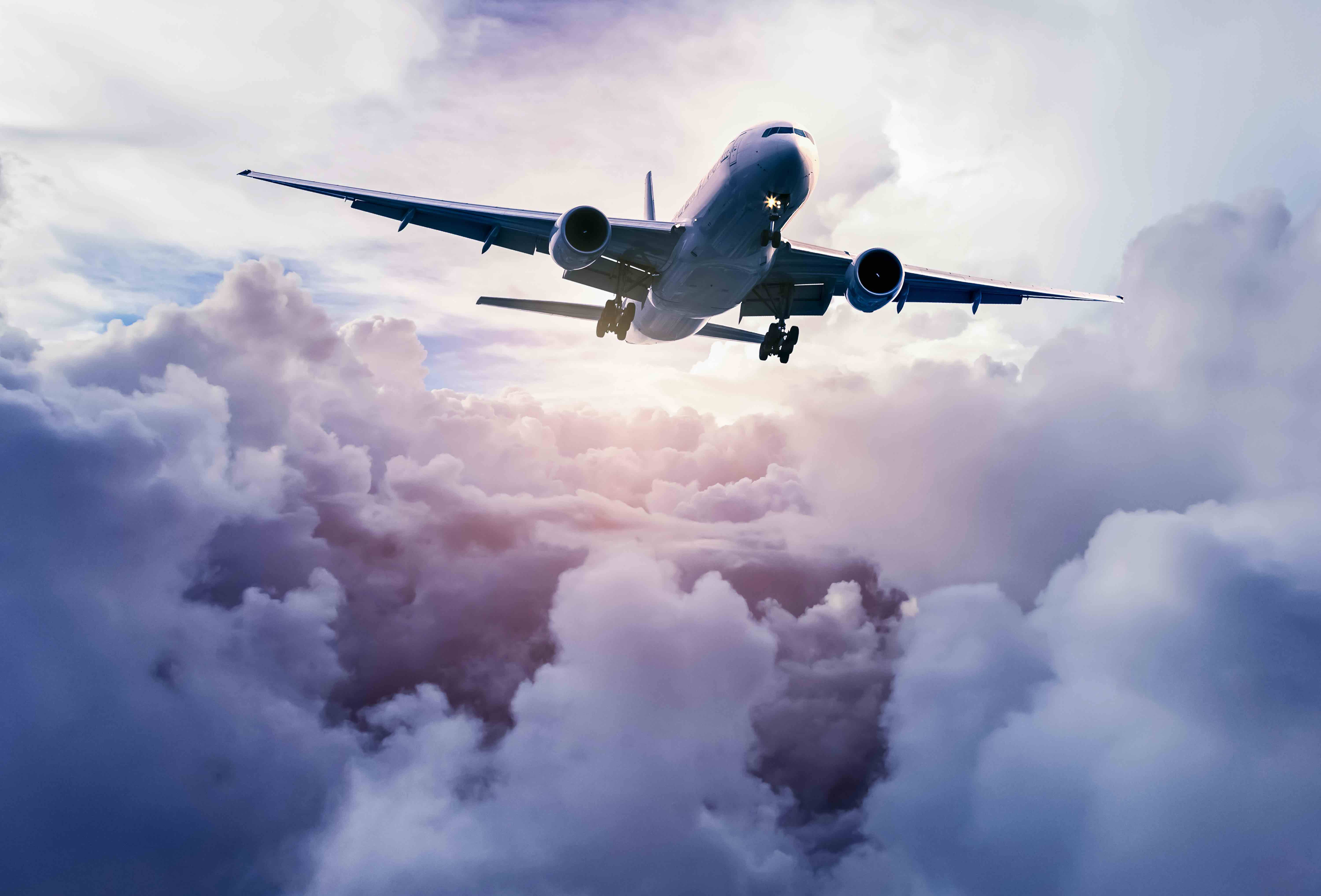 飛機 桌布 壁紙 — 一架大型客機在柔軟的雲層上方翱翔，沐浴在柔和的金色日出光芒中。