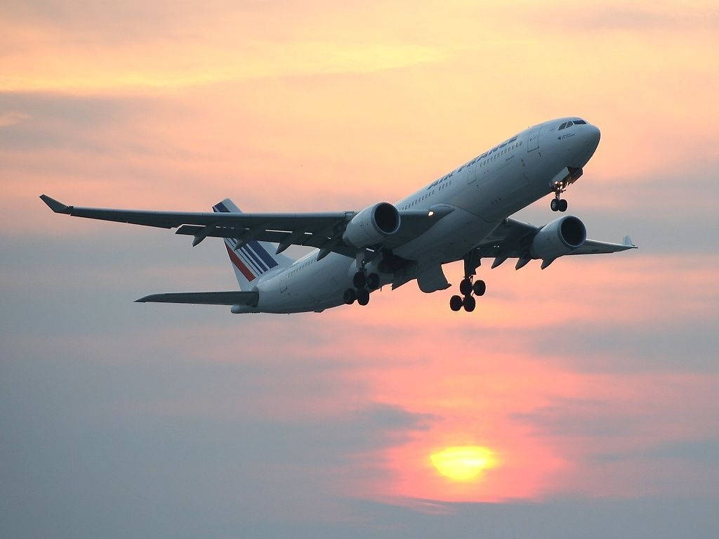 Plane 桌布 壁紙 — 一架大型客機在橙粉紅色的雲彩映襯下，於充滿活力的日落天空中下降。
