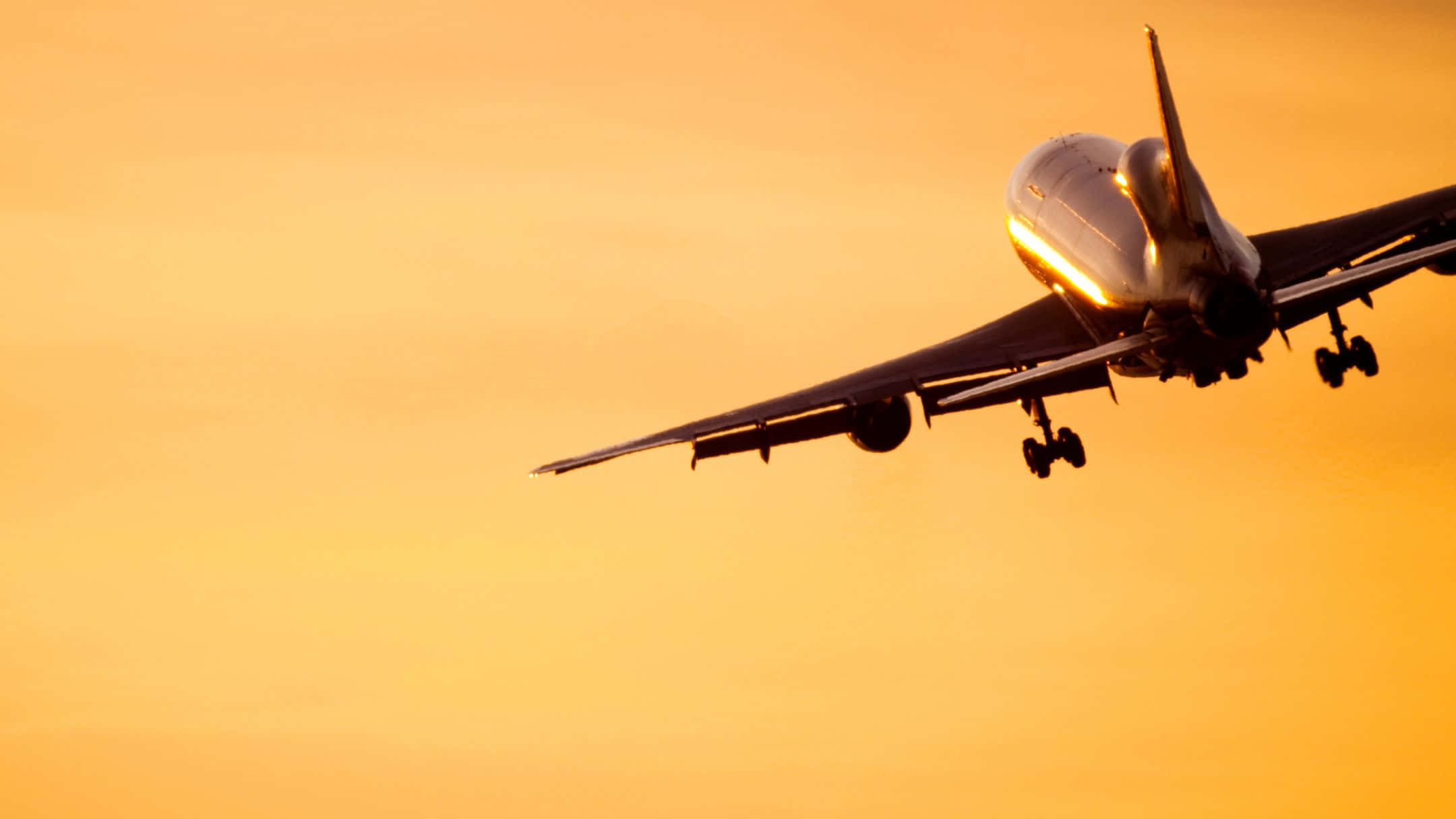 日落 桌布 壁紙 — 一架大型客機在溫暖的金色日落天空中攀升，起落架仍然伸出。