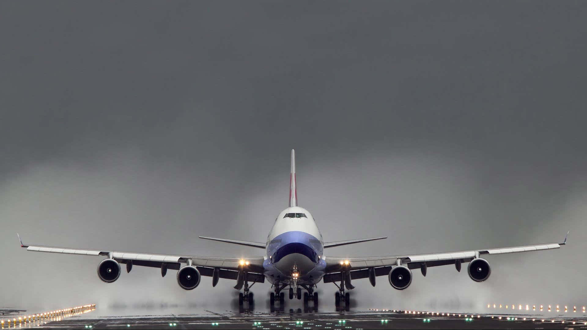 747 Airplane 桌布 壁紙 — 一架大型客機在潮濕的跑道上接近，天空灰暗沉重，跑道燈光在下方閃爍。