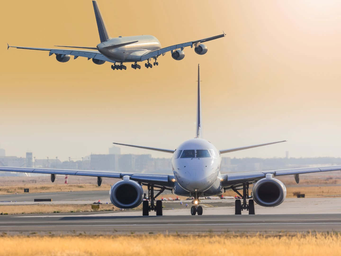 飛機 桌布 壁紙 — 一架大型客機在跑道上滑行，另一架飛機正準備降落，背景是金色的日落天空。