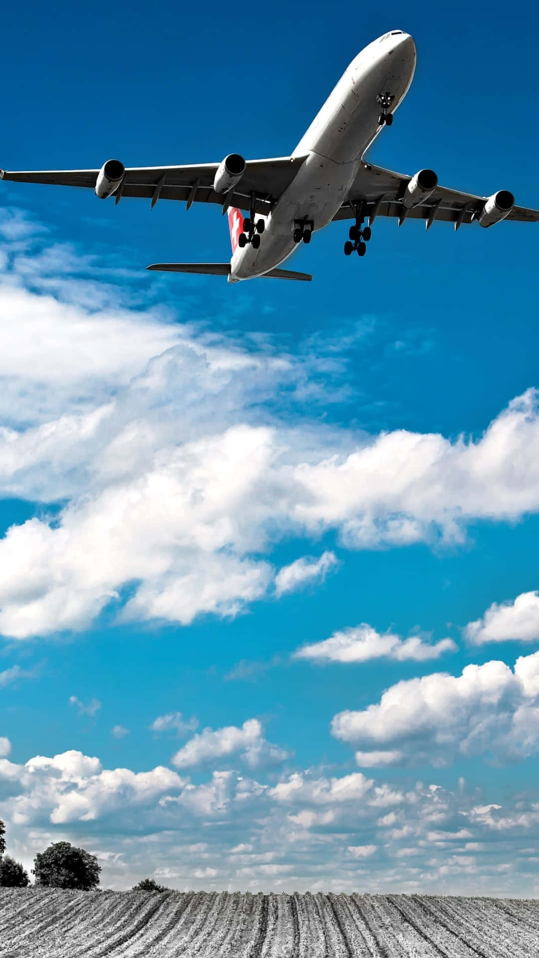 Airlines 桌布 壁紙 — 一架大型客機放下起落架，在一片犁過的田野上空，對著充滿蓬鬆白雲的鮮豔藍天下降。