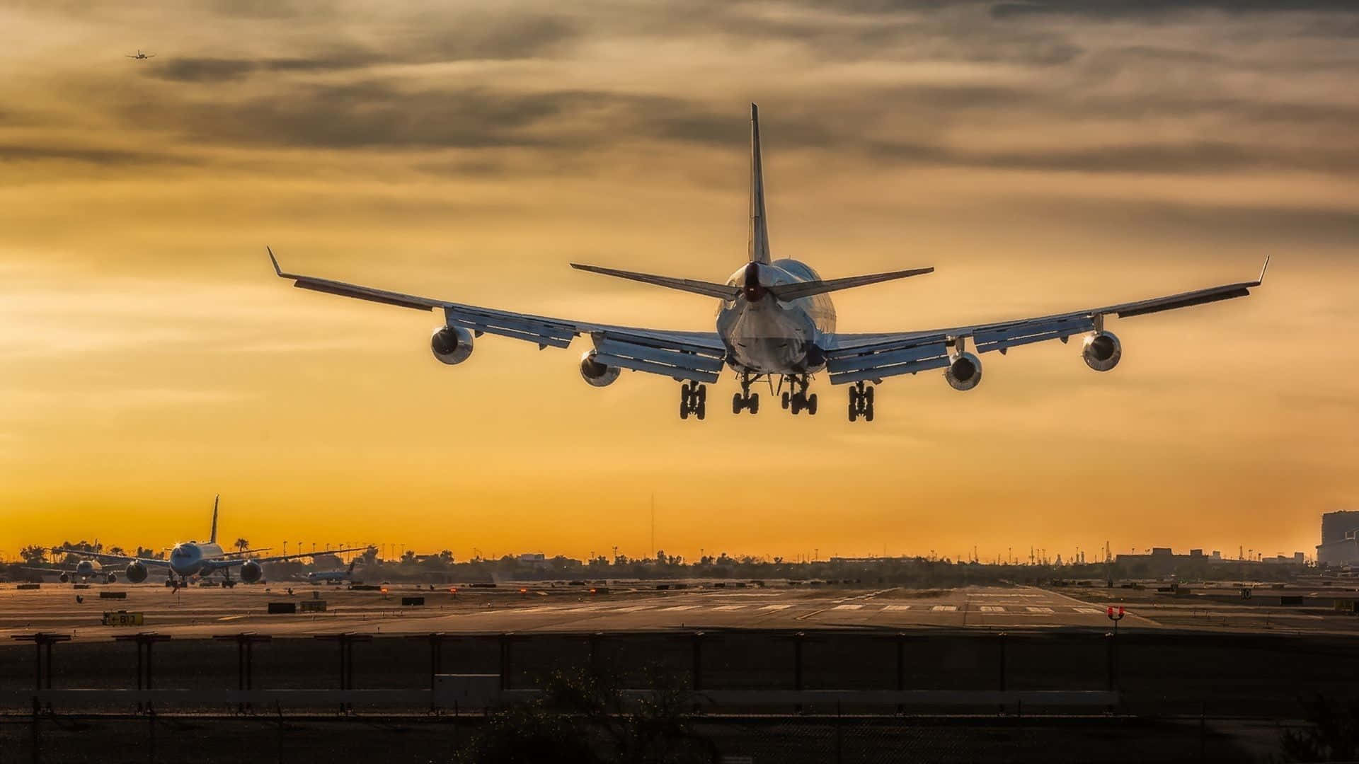 HD Plane 桌布 壁紙 — 一架大型客機正降落在被金色夕陽光芒籠罩的機場跑道上，天空中的雲彩呈現橙色和黃色條紋。