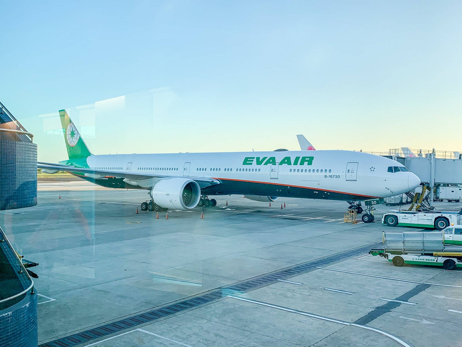 Airport 桌布 壁紙 — 一架大型白色EVA Air客機在黃金時段停泊在機場閘口，附近有地勤人員和設備。