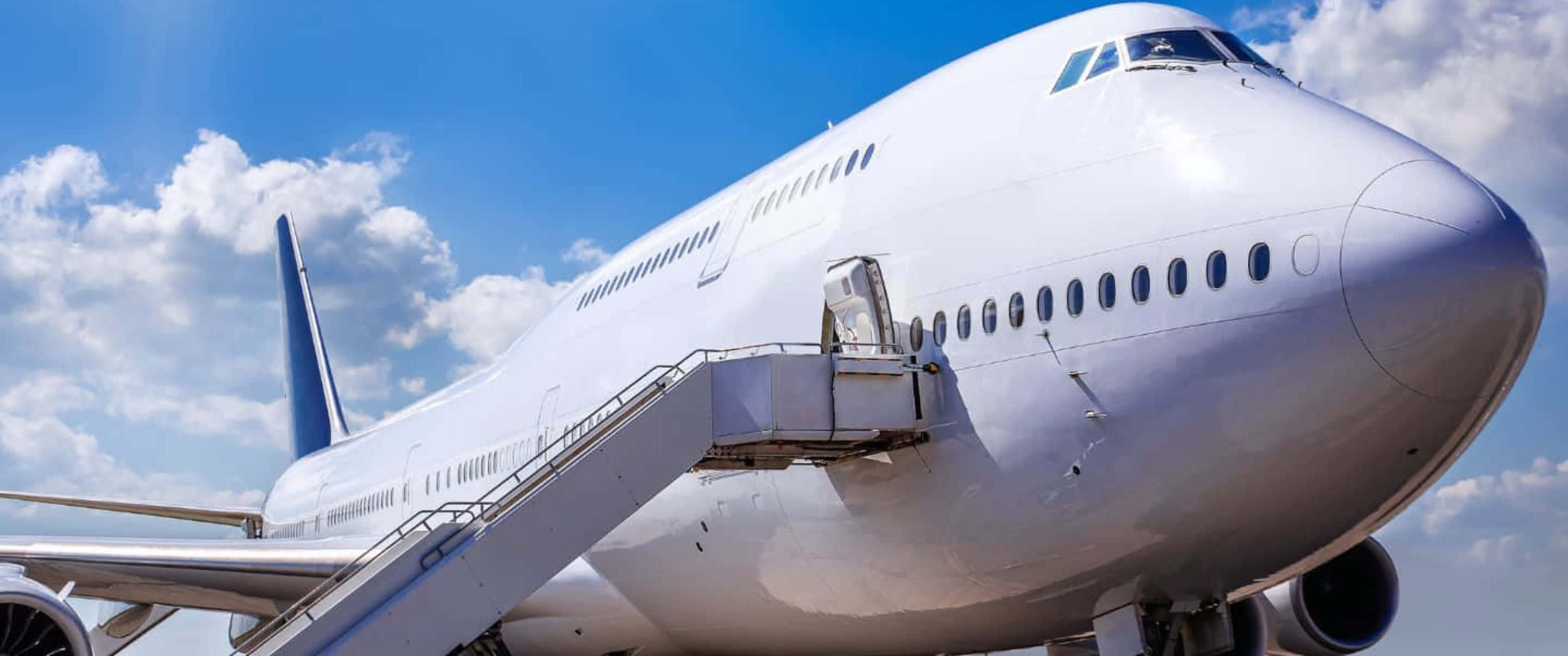 飛機 桌布 壁紙 — 一架大型白色客機連接著登機梯，矗立在點綴著蓬鬆白雲的明亮藍天下。