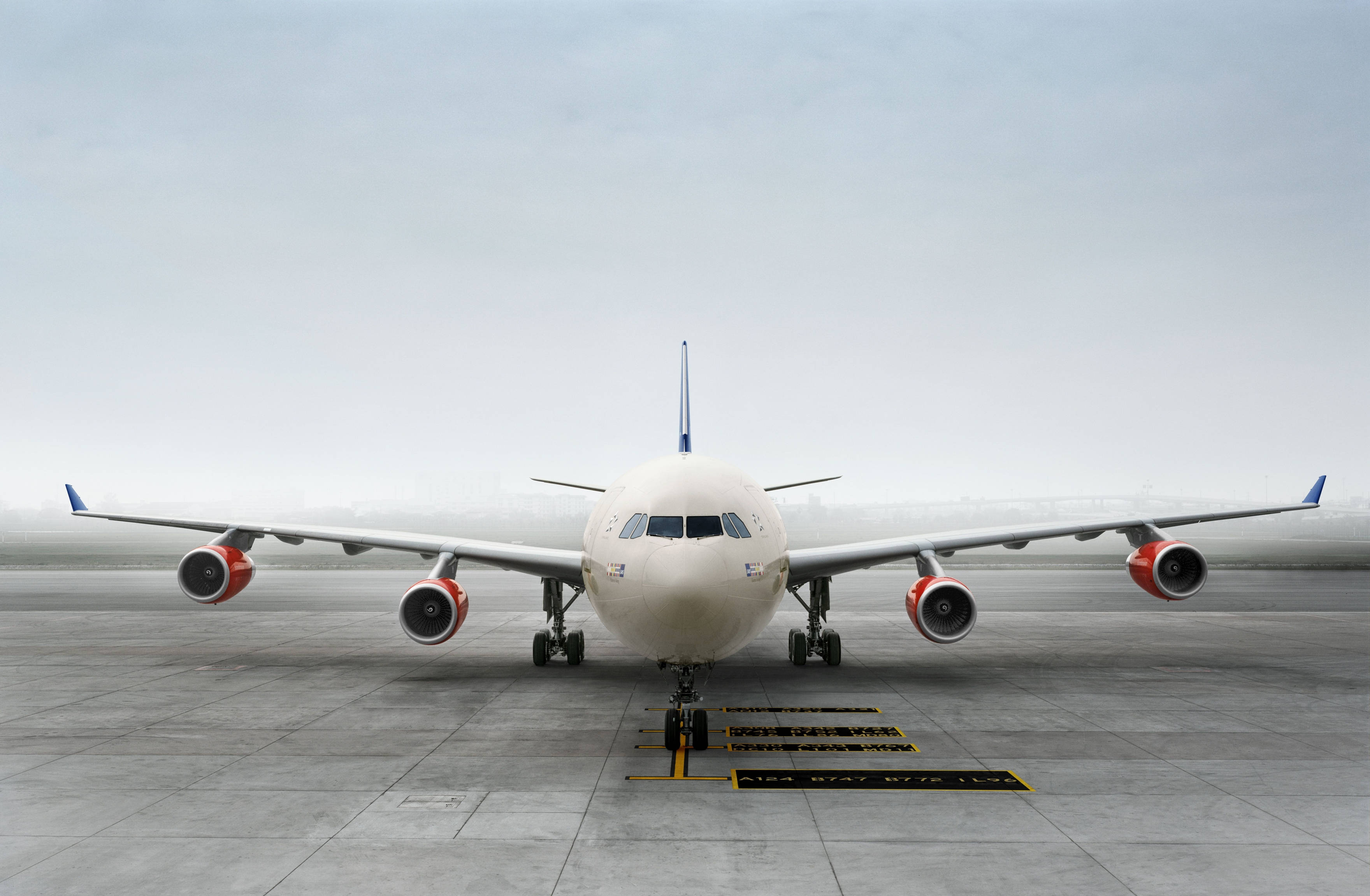 Airport 桌布 壁紙 — 一架大型白色客機配備紅色引擎，停放在灰色停機坪中央，天空多雲。