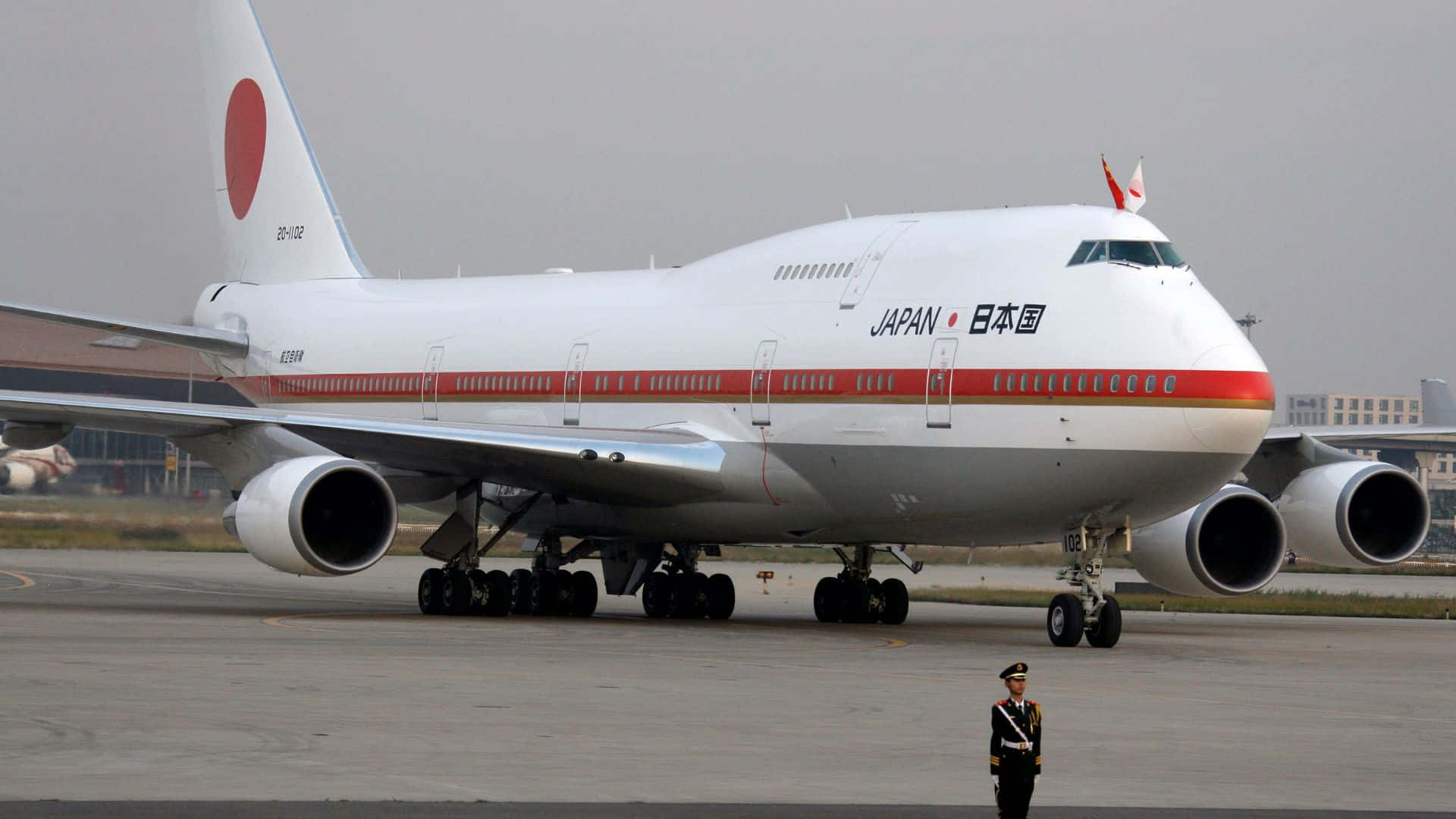 1920x1080 Jumbo Jets 桌布 壁紙 — 一架大型白色日本總統專用波音747停在機場停機坪上，附近有一名身穿制服的警衛站崗。