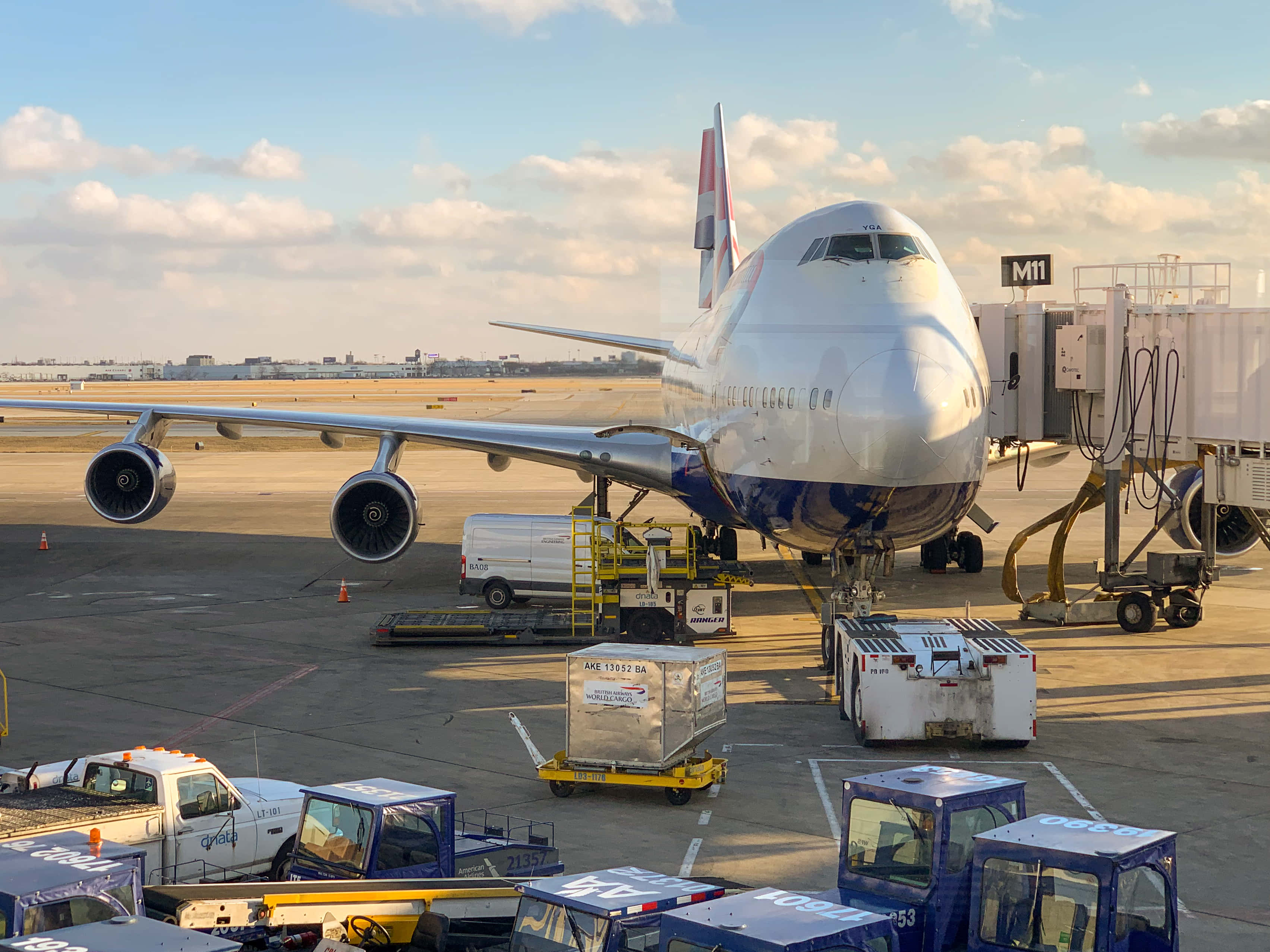 Airport 桌布 壁紙 — 一架大型白色貨機停泊在機場閘口，周圍有地勤人員車輛和設備，天空部分多雲。