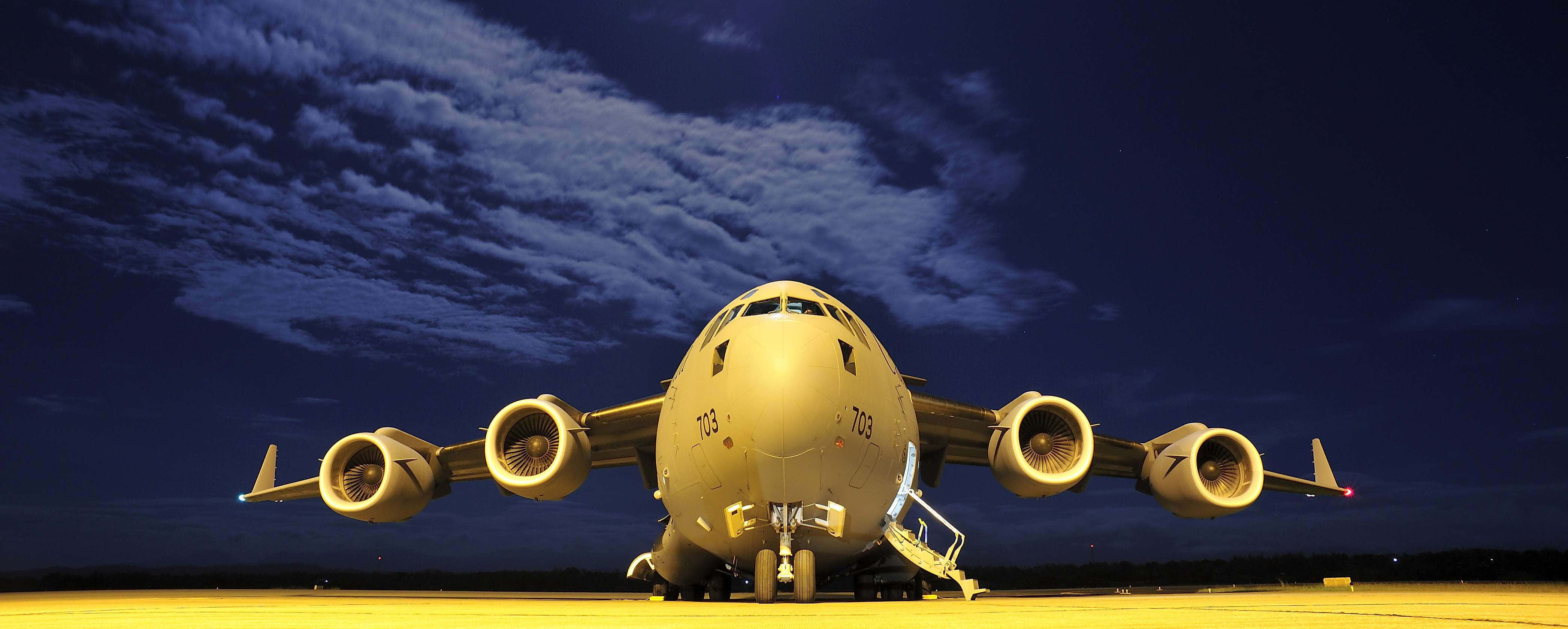 Air Force 桌布 壁紙 — 一架大型軍用運輸機在深藍色夜空下，散雲點綴，停泊在燈光溫暖的停機坪上。