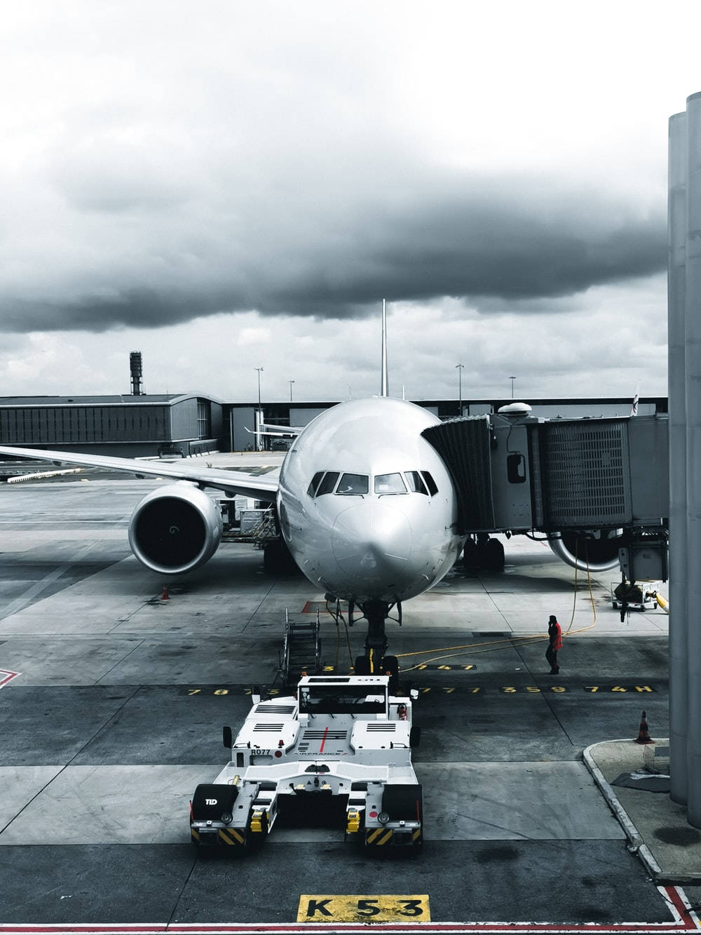 Plane 桌布 壁紙 — 一架大型銀色飛機停泊在機場閘口，天空陰沉密佈，附近有地勤人員和牽引車。