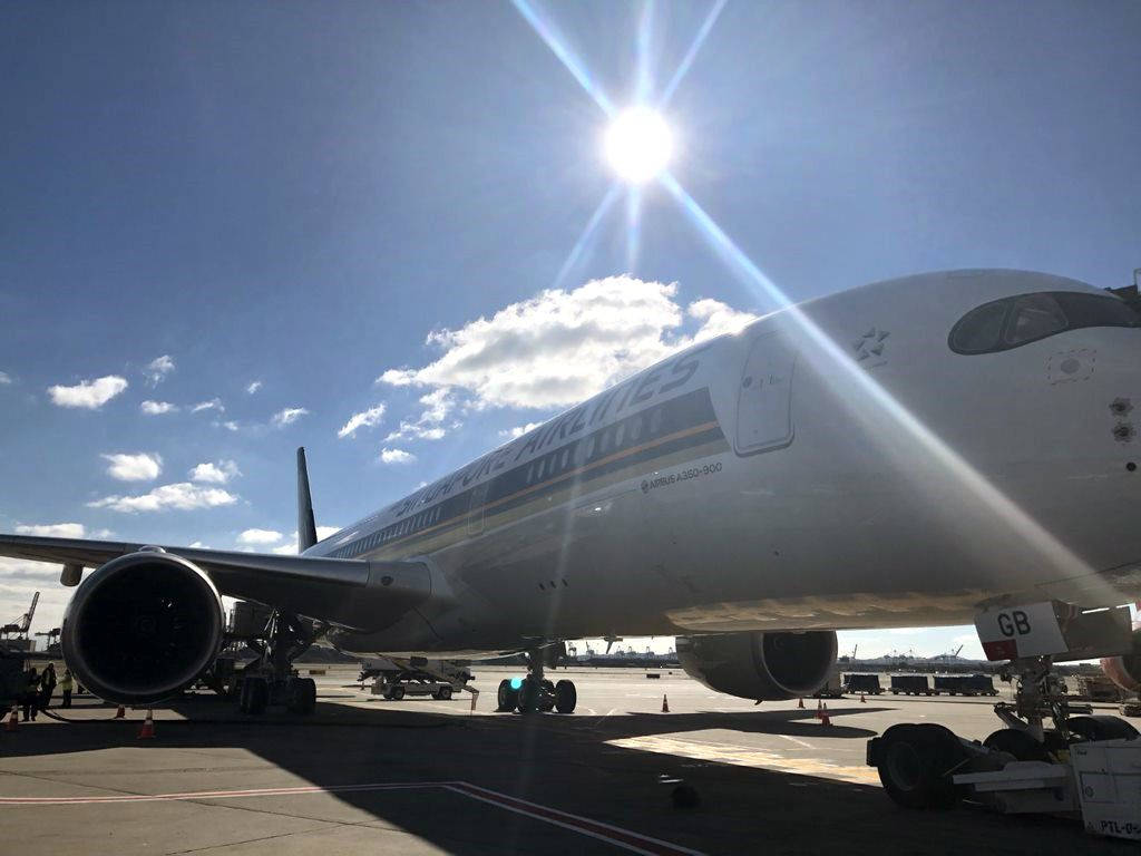 Airport 桌布 壁紙 — 一架大型阿聯酋航空空中巴士A350-900停泊在陽光明媚的機場停機坪上，上方有明亮的太陽耀斑和散落的雲朵。