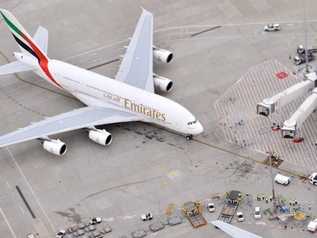 Airport 桌布 壁紙 — 一架大型阿聯酋航空空中巴士A380停泊在機場閘口，周圍有地勤人員和服務車輛的鳥瞰圖。