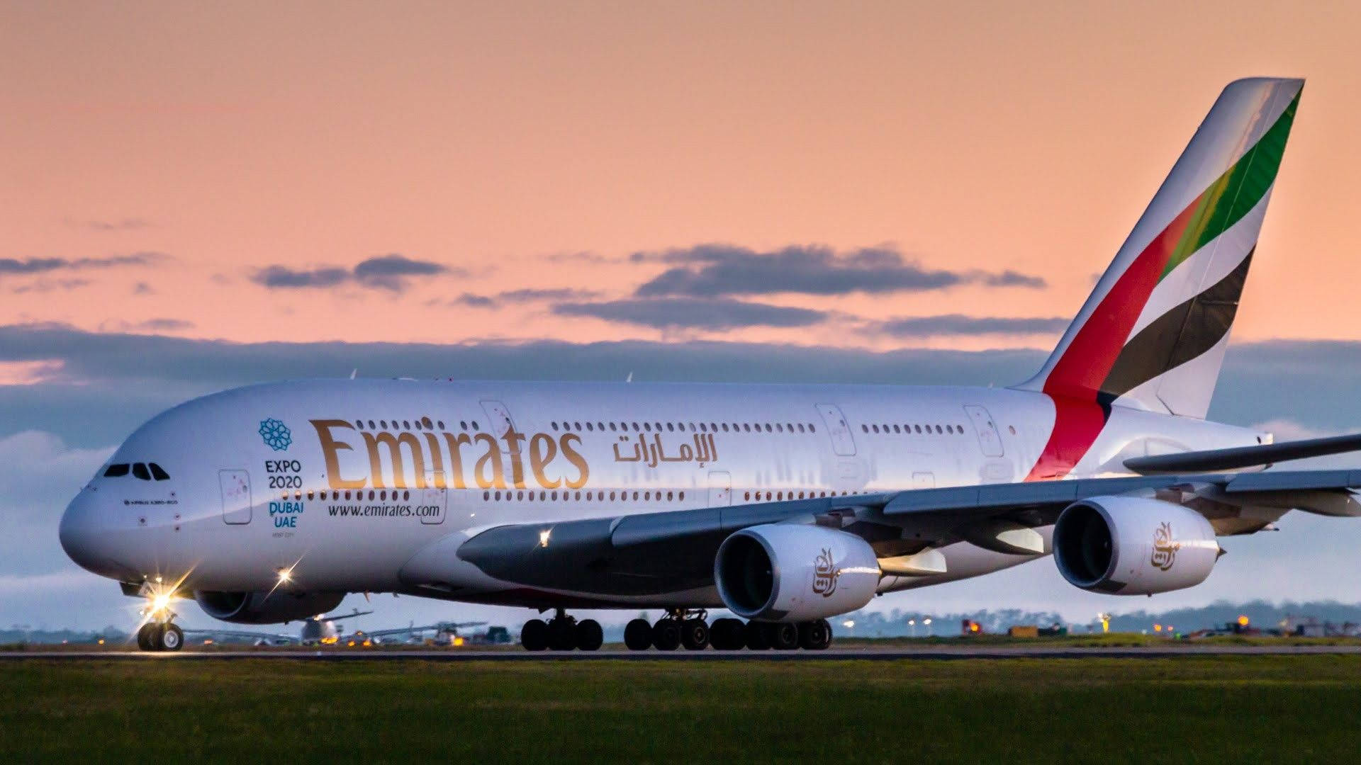 飛機 桌布 壁紙 — 一架大型阿聯酋航空空中巴士A380在黃昏時分在跑道上滑行，背後是粉紅色和橙色的天空。