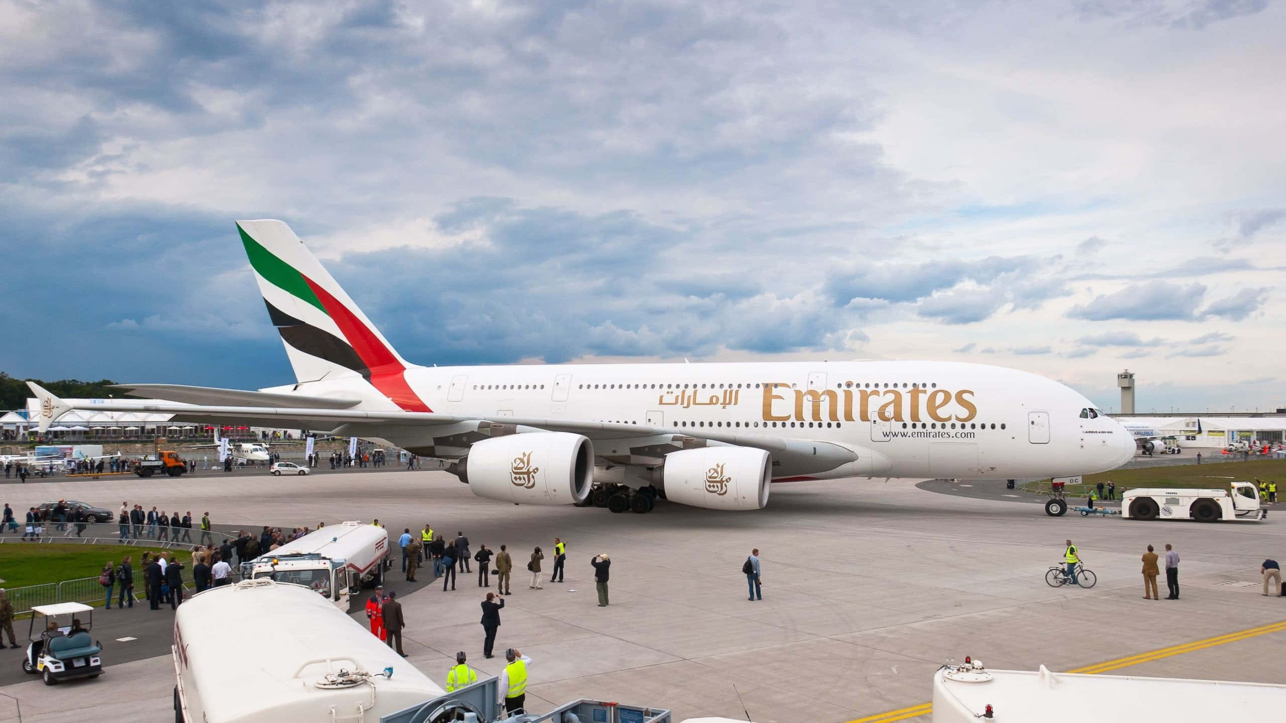 桌布 壁紙 — 一架大型阿聯酋航空空中巴士A380在陰天停泊在機場停機坪，附近有地勤人員和觀眾。