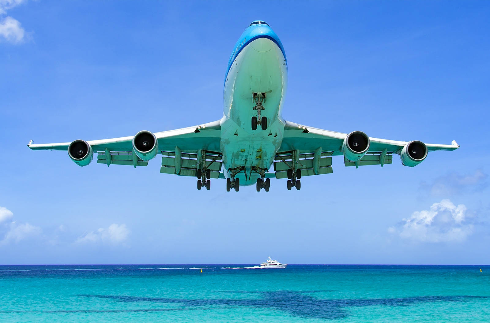飛機 桌布 壁紙 — 一架大型青綠色飛機低飛過充滿活力的青綠色海洋，下方可見一艘白色小船。