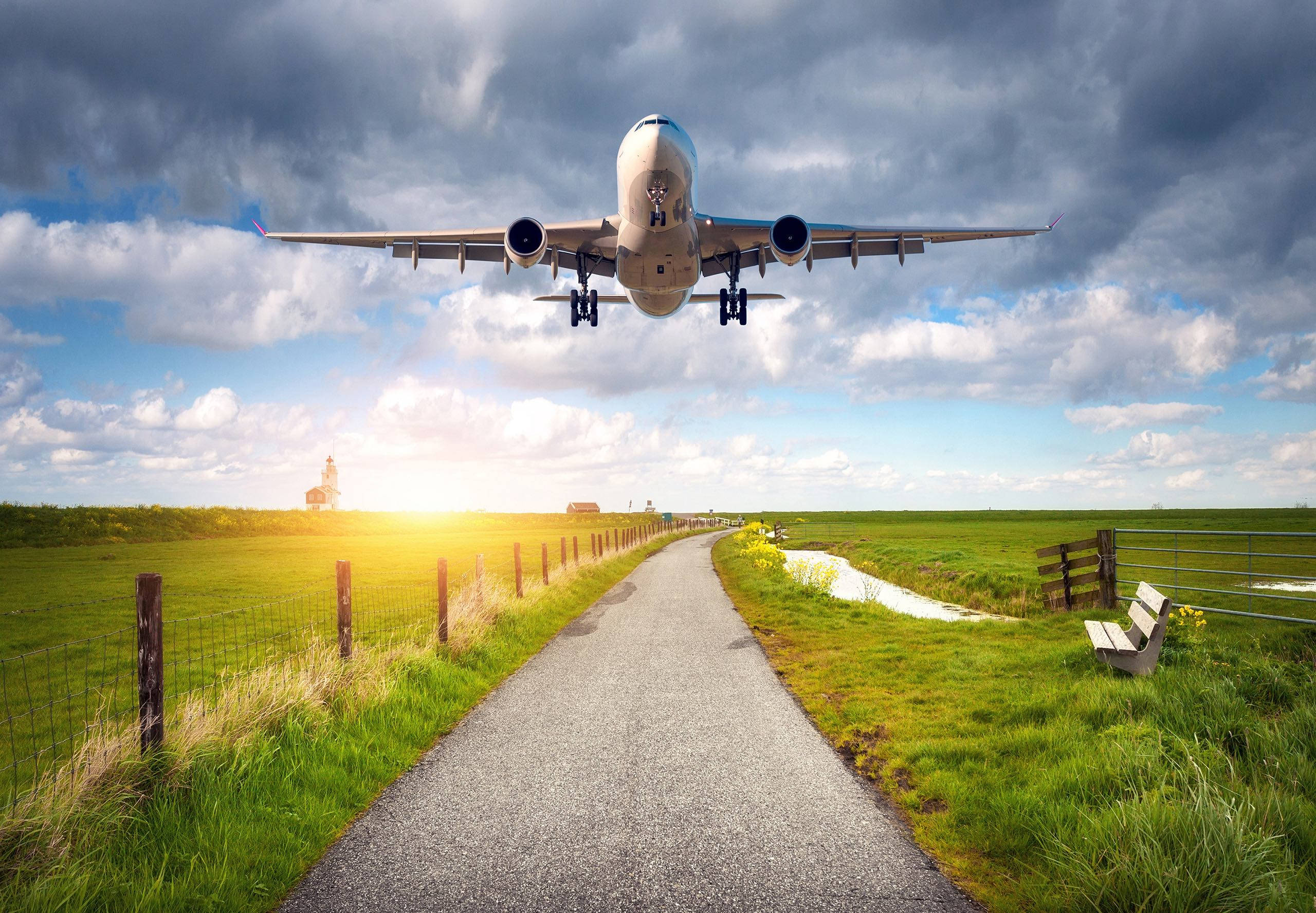 Road 桌布 壁紙 — 一架大型飛機低飛過鄉村小徑，金色夕陽光線穿過戲劇性的雲層。