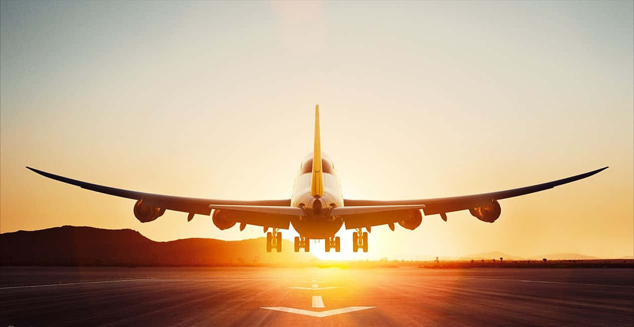 747 Airplane 桌布 壁紙 — 一架大型飛機停在跑道上，夕陽西下，金色光芒在背後閃耀，遠處有山丘。
